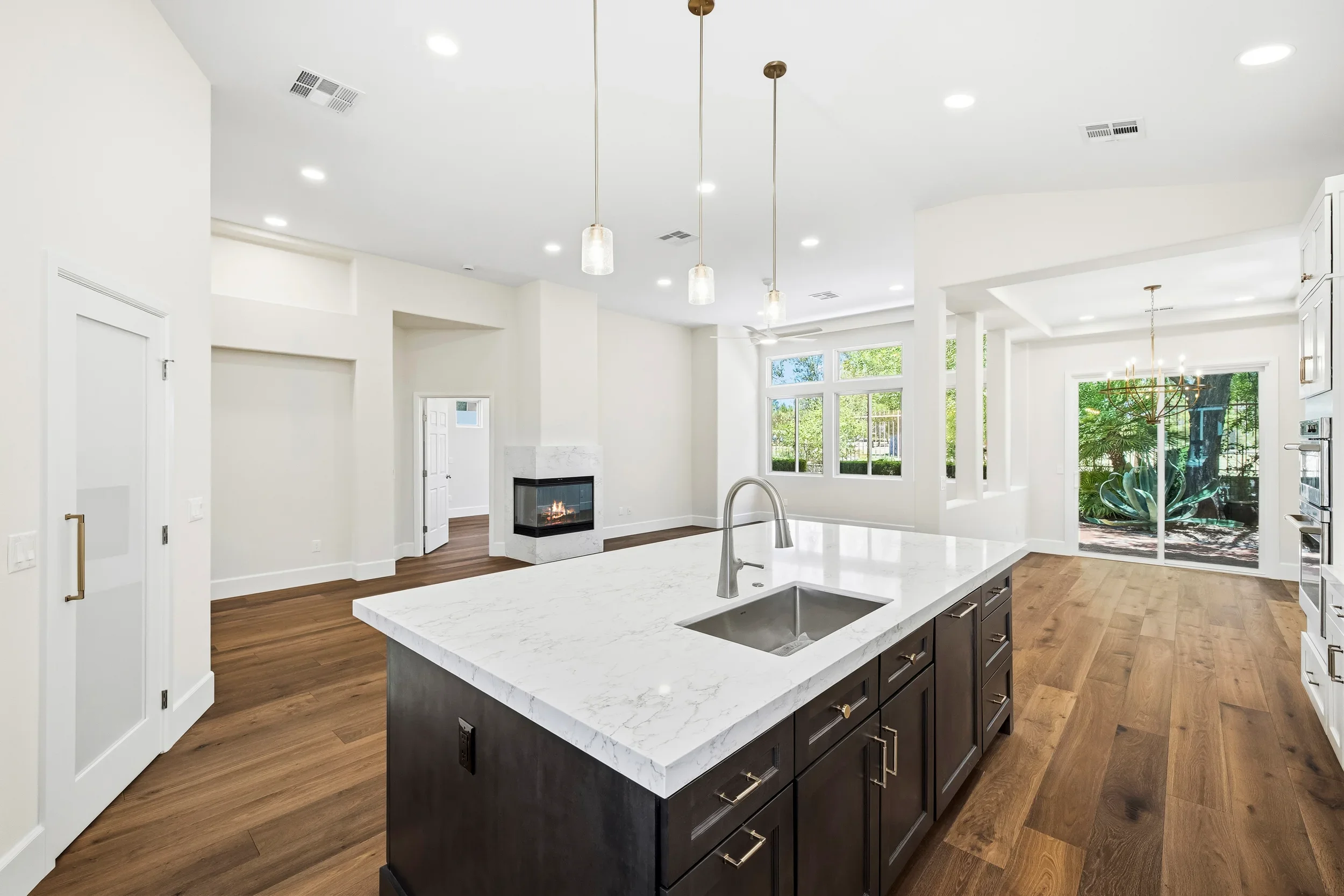 Open kitchen with marble island, dark cabinets, hardwood floors, and fireplace