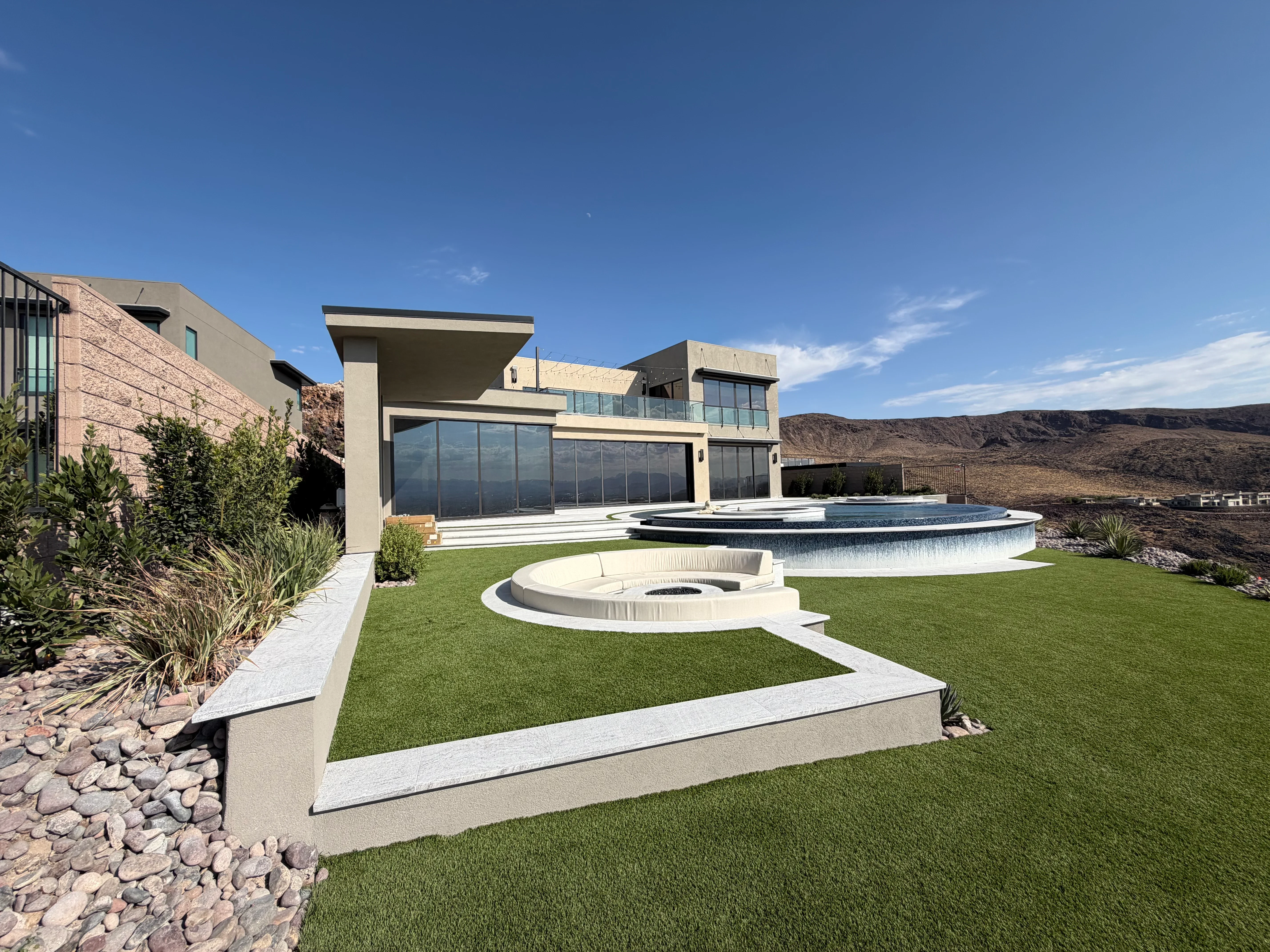 Modern home with stucco exterior, large windows, synthetic lawn, concrete patios, fire pit, and pool with spa
