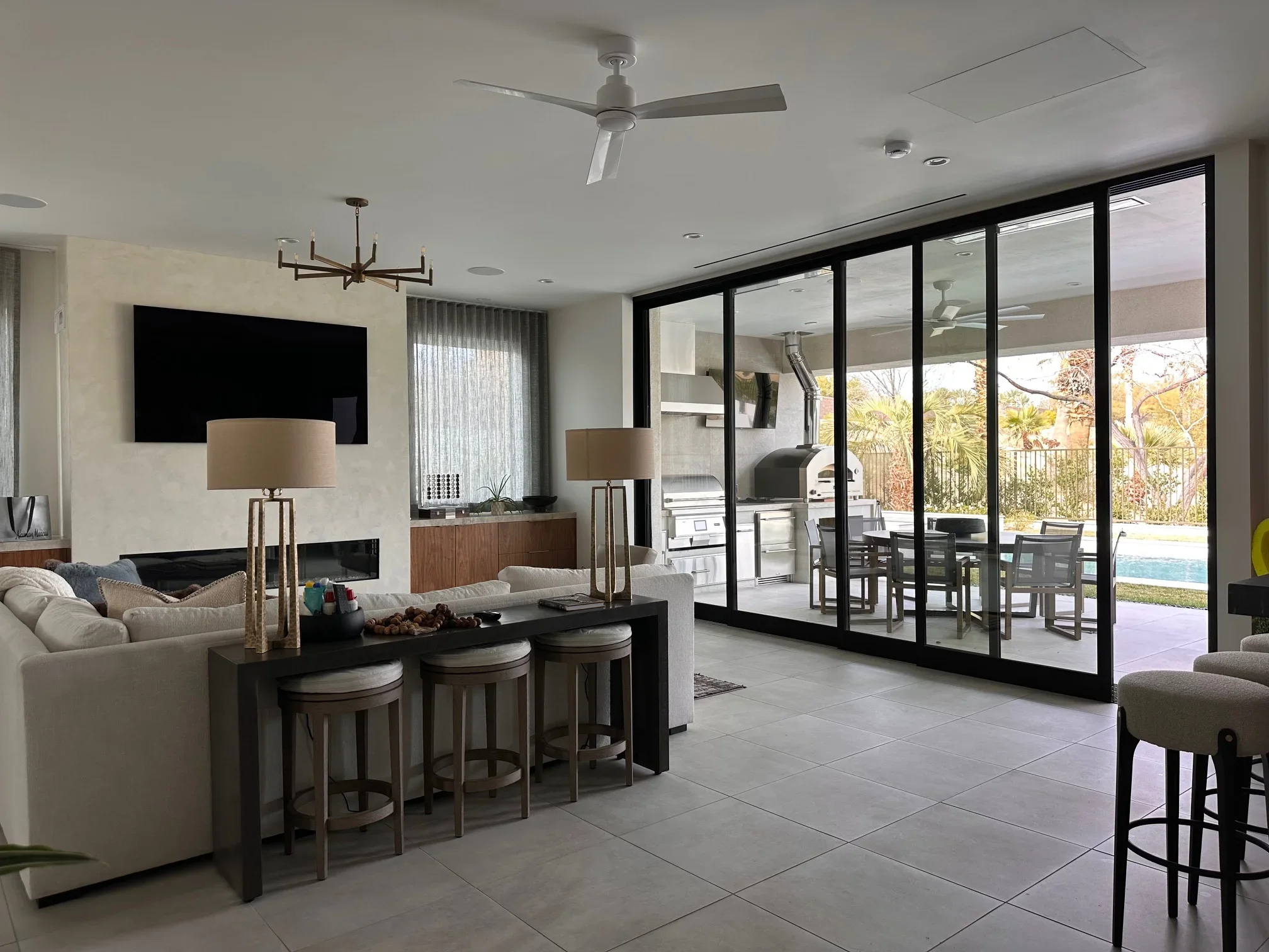 Modern living room with black-framed glass doors, tile flooring, fireplace, and open patio view