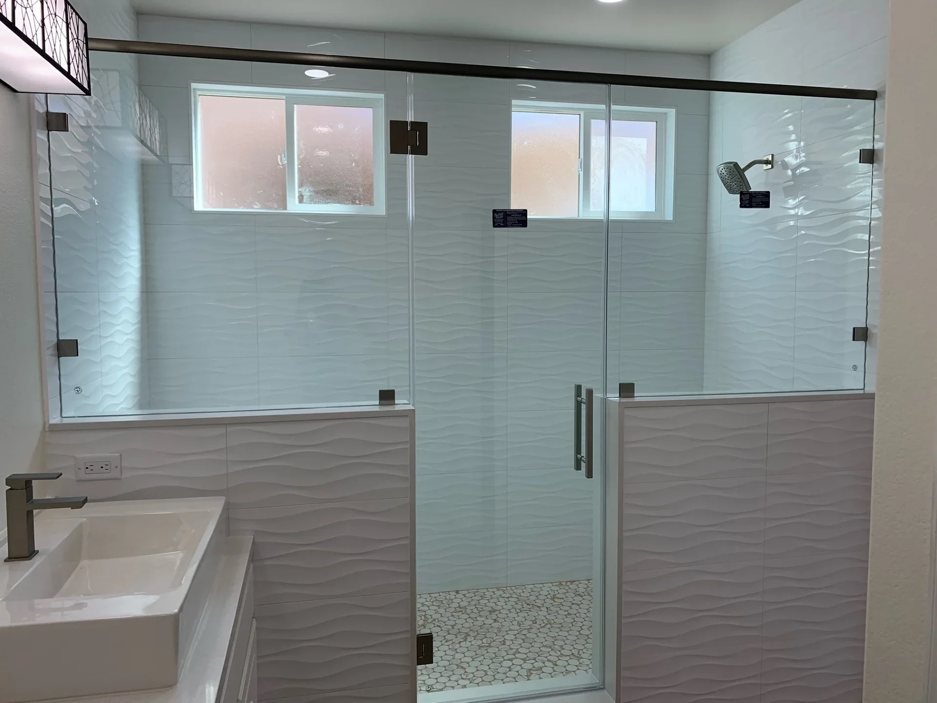 Frameless glass shower with wave-pattern tile surround and pebble stone floor in renovated bathroom