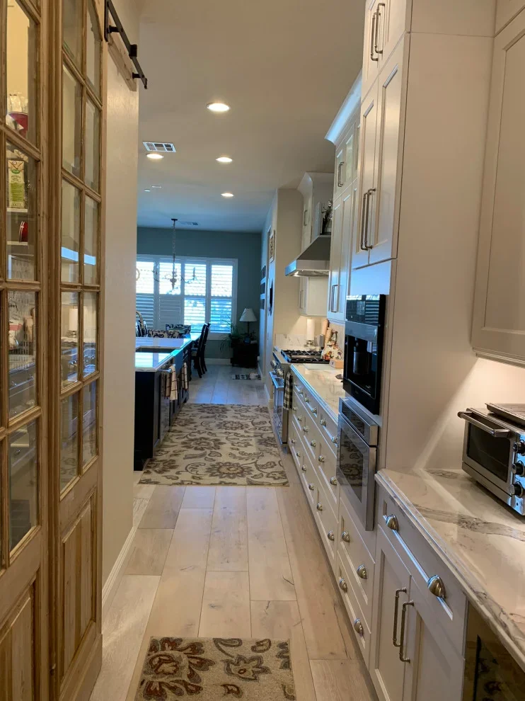 White kitchen with marble counters, stainless steel appliances, wood flooring, and open great room view