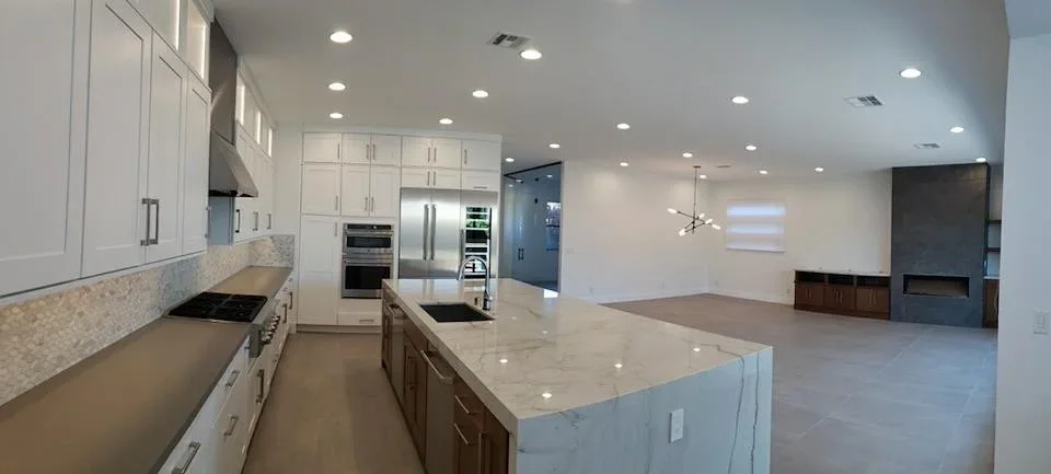 Modern kitchen with white cabinets, stainless steel appliances, quartz island, and recessed lighting