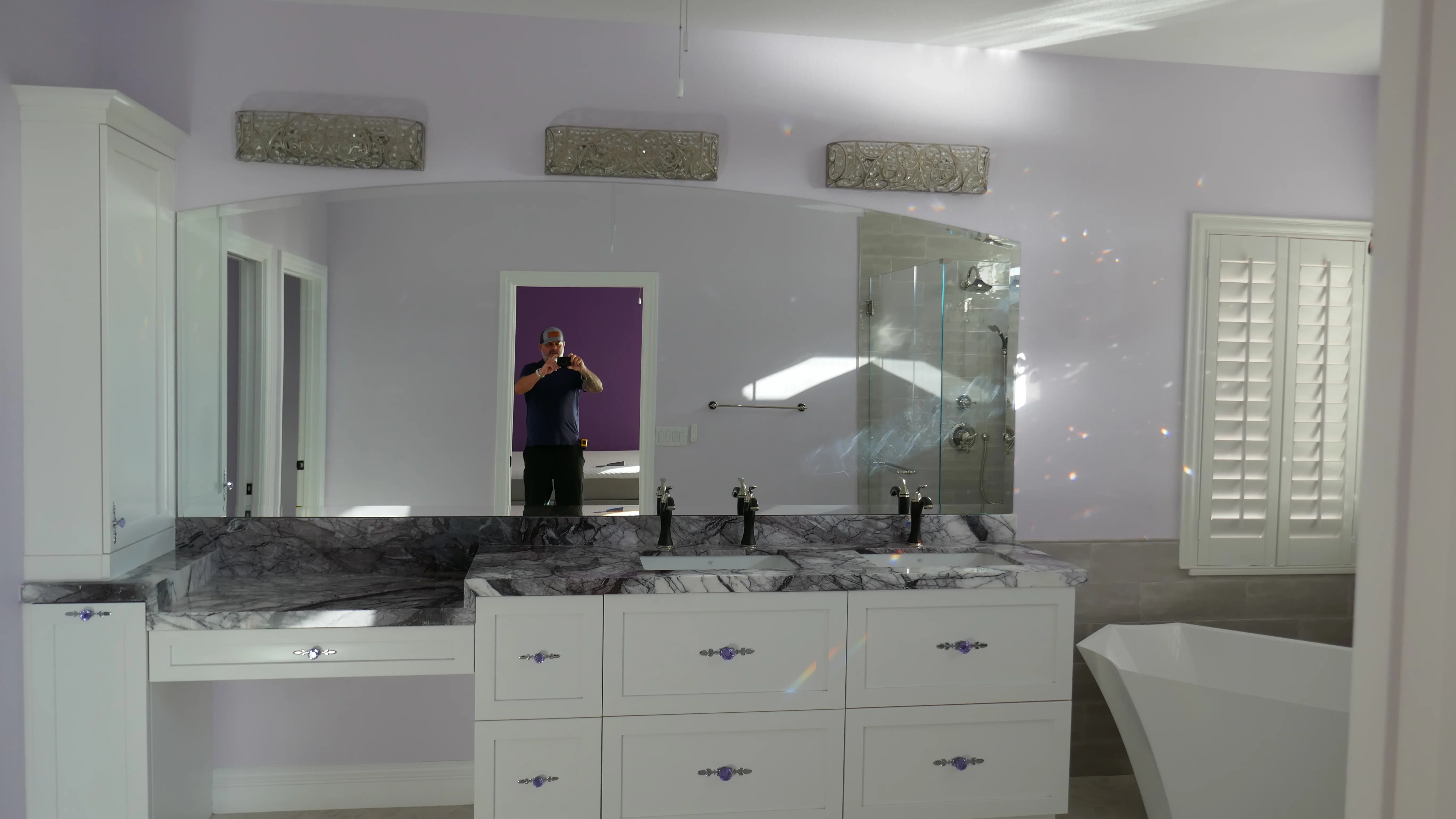 Master bathroom with marble double vanity, white cabinetry, frameless glass shower, and large mirror