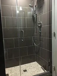 Frameless glass shower enclosure with dark gray subway tile walls and stone floor