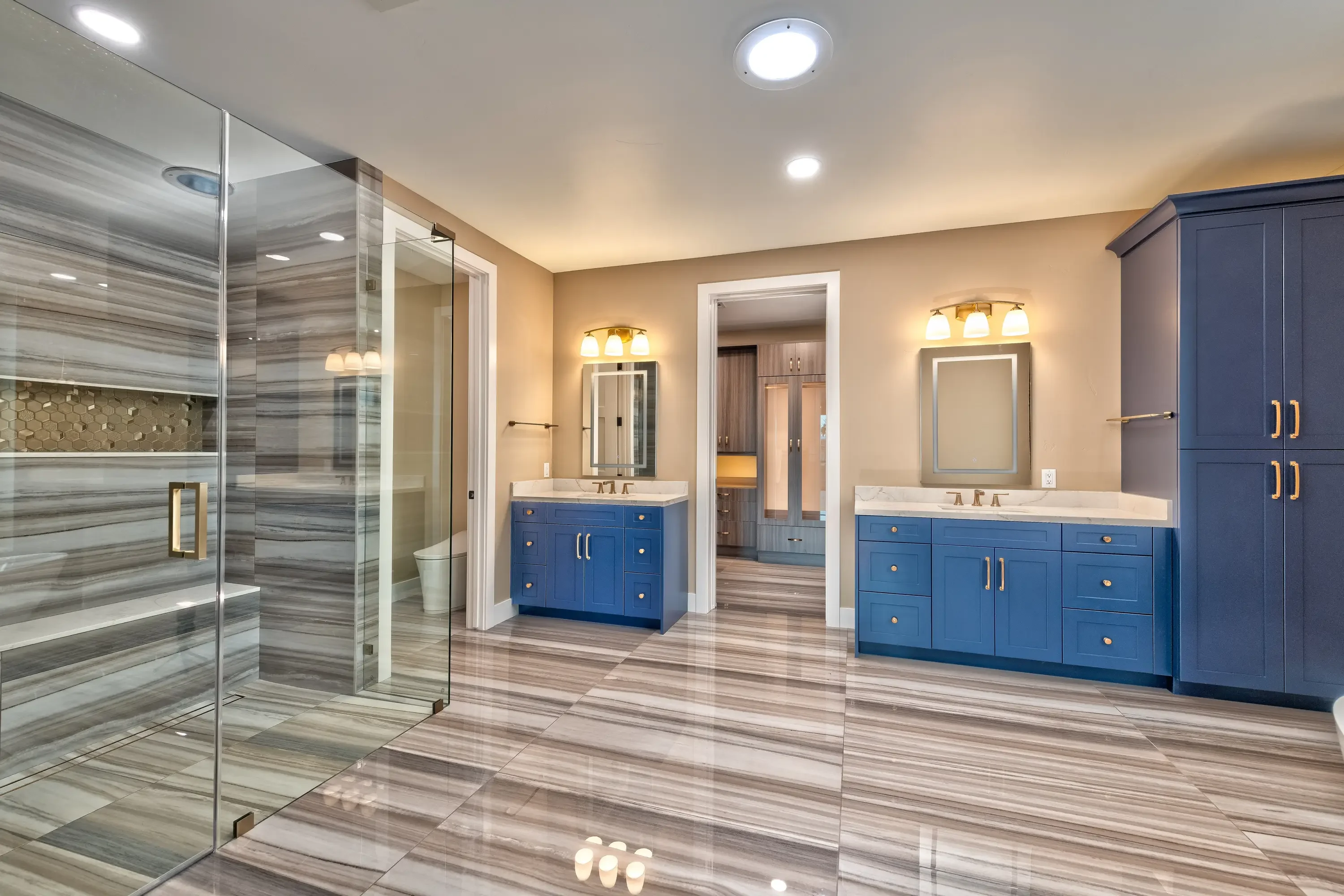 Dual blue vanities, frameless shower enclosure, quartz counters, wood-look tile flooring