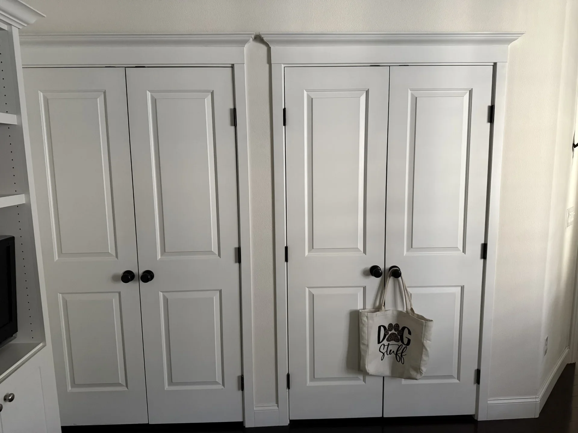 Four white six-panel closet doors with black hardware and trim molding