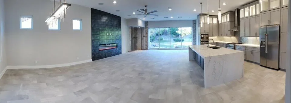 Open kitchen and living room with white cabinetry, marble island, stainless appliances, and blue tile fireplace