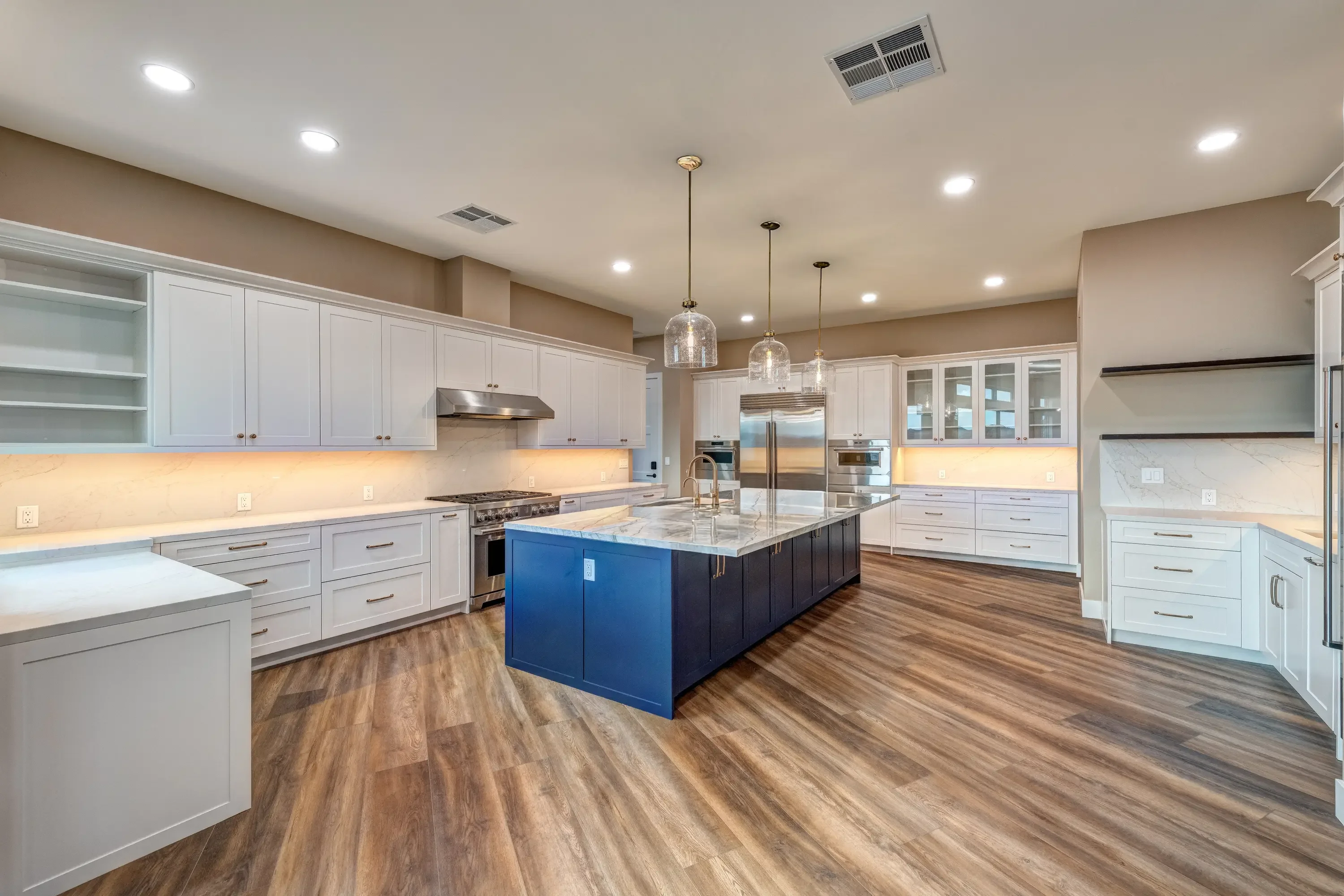 White kitchen cabinetry with blue island, marble counters, stainless steel appliances, and wood flooring