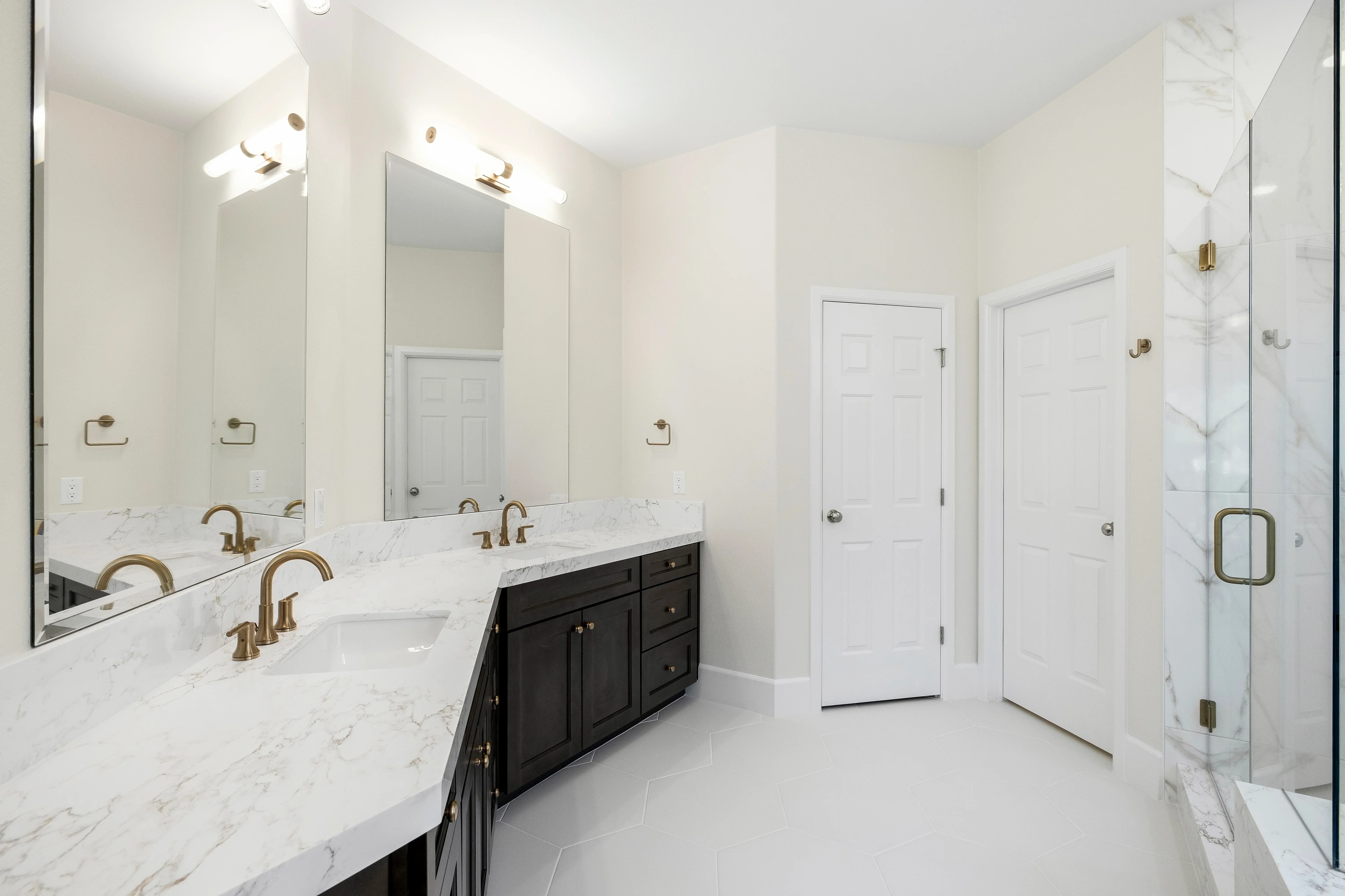 Luxury bathroom with dual marble vanity, black cabinetry, gold fixtures, and frameless glass shower enclosure