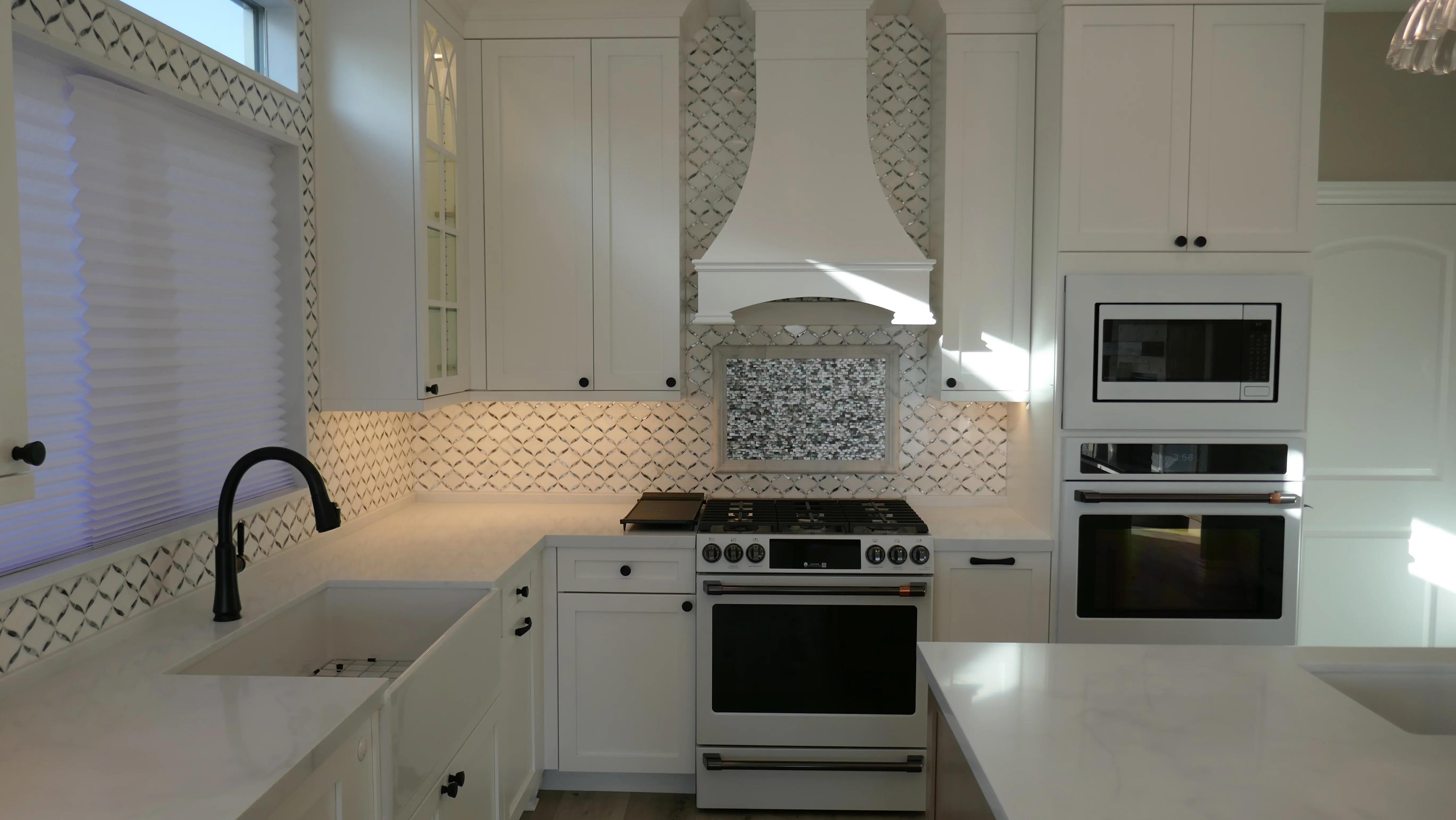 White kitchen with geometric tile backsplash, quartz counters, stainless steel appliances, and custom range hood