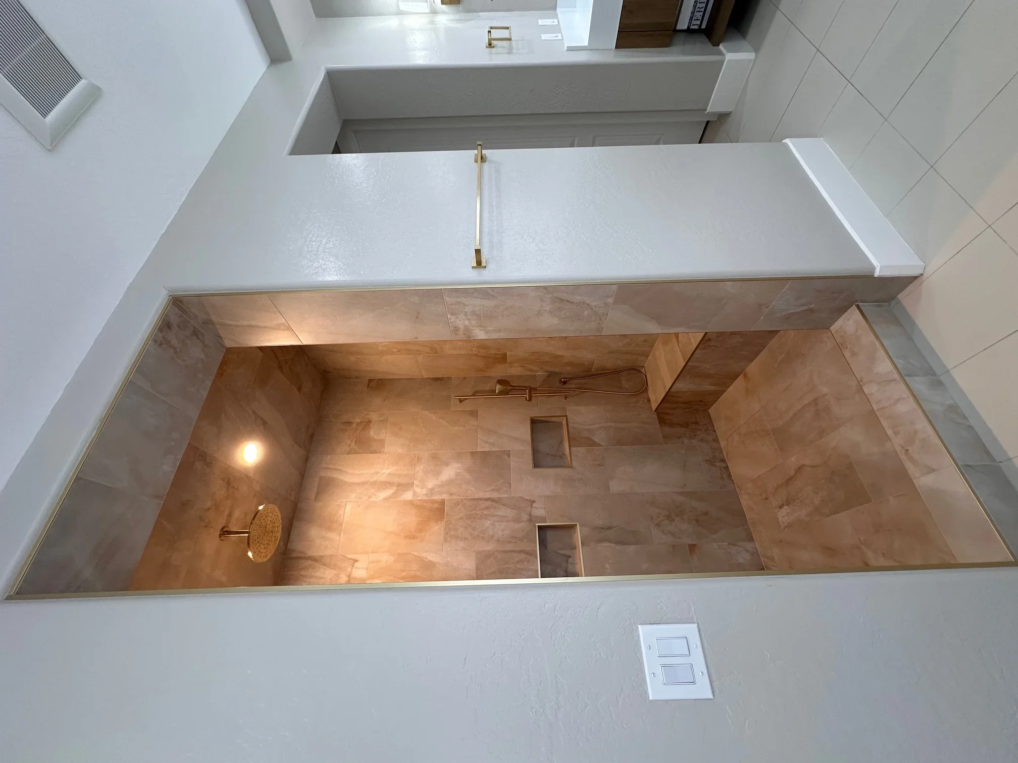 Walk-in shower with large-format porcelain tile, gold showerhead, and white quartz vanity