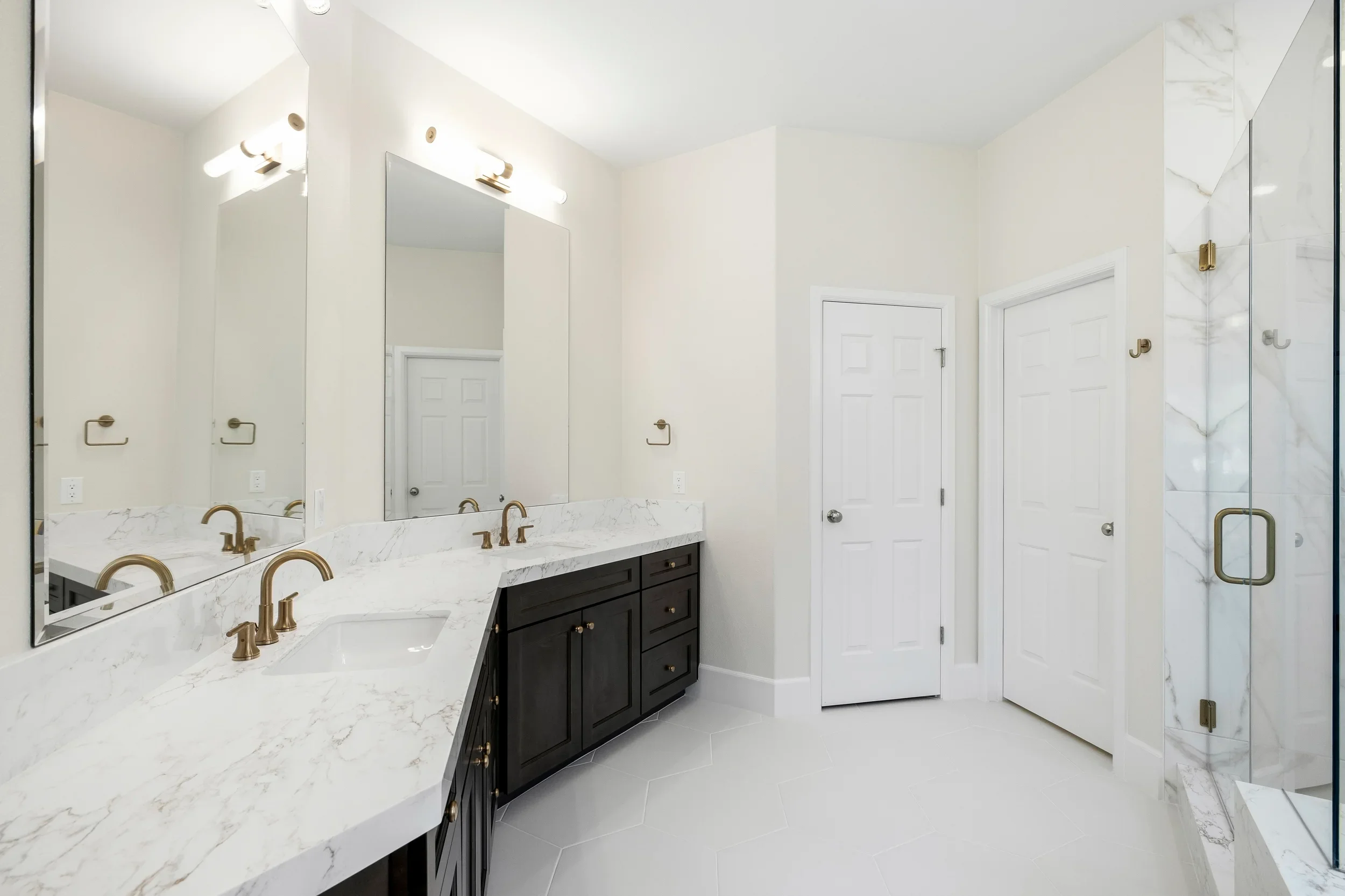Dual vanity bathroom with marble countertops, black cabinetry, brass fixtures, and frameless glass shower enclosure