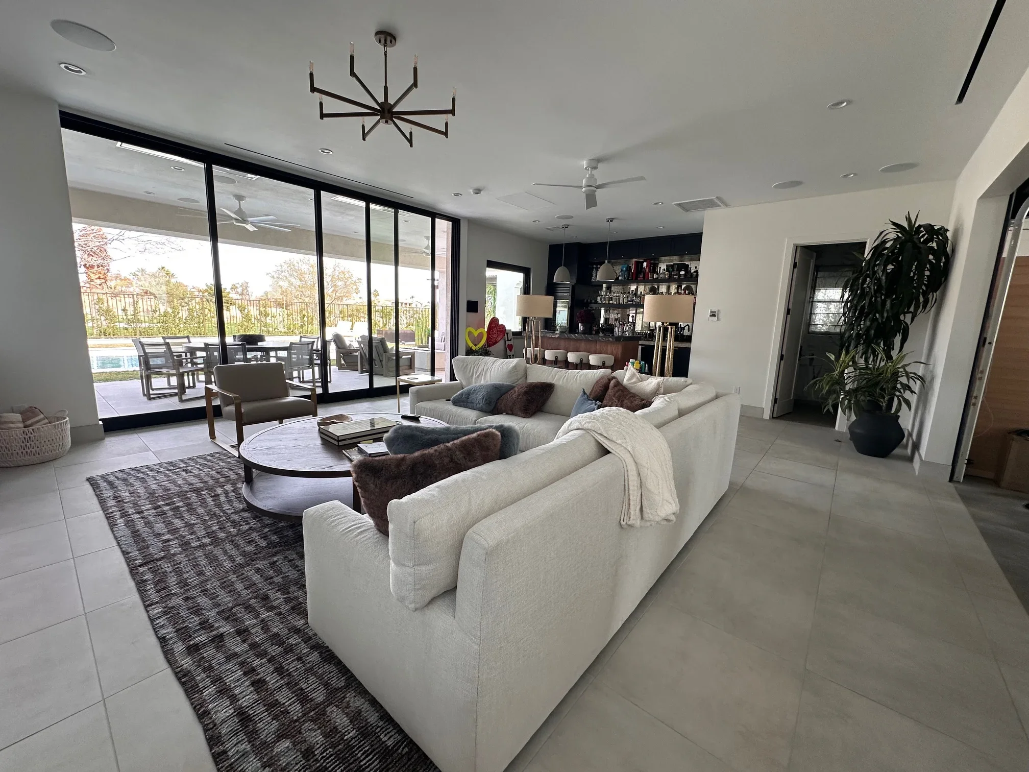 Modern living room with white sectional sofa, concrete floors, black-framed glass doors, and pool view