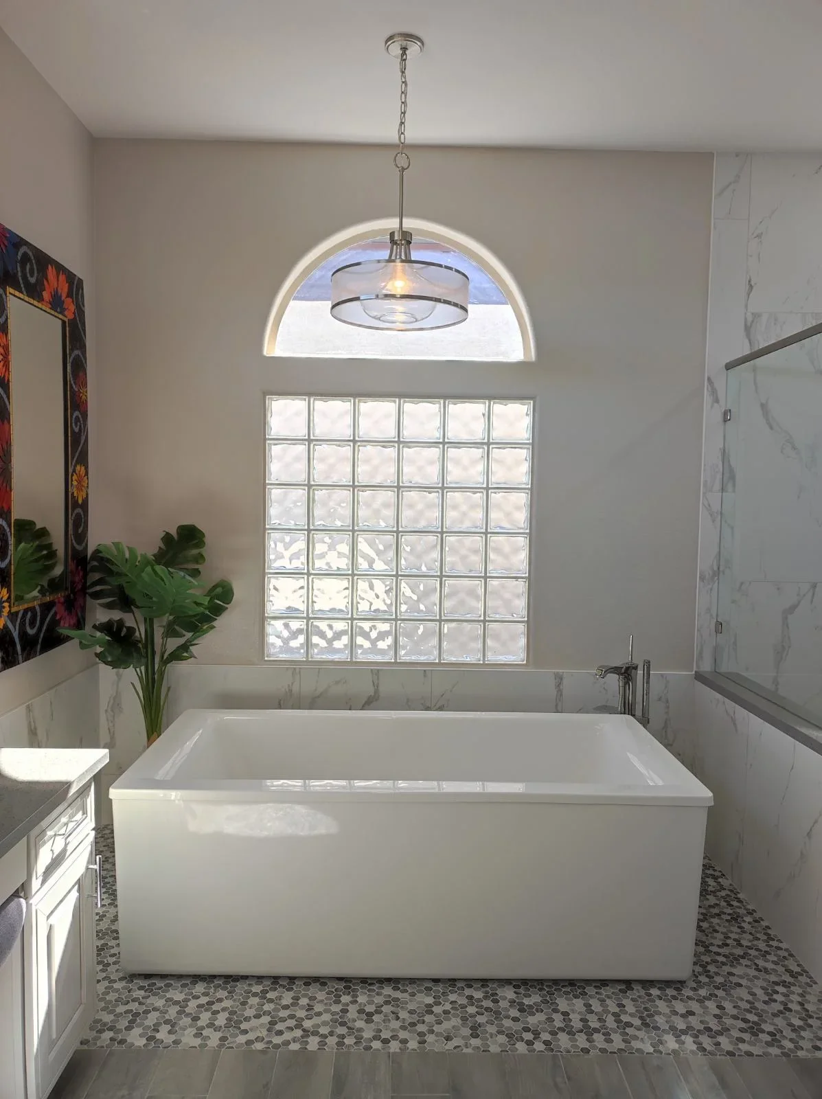 Freestanding soaking tub with marble tile walls, glass block window, and pendant lighting