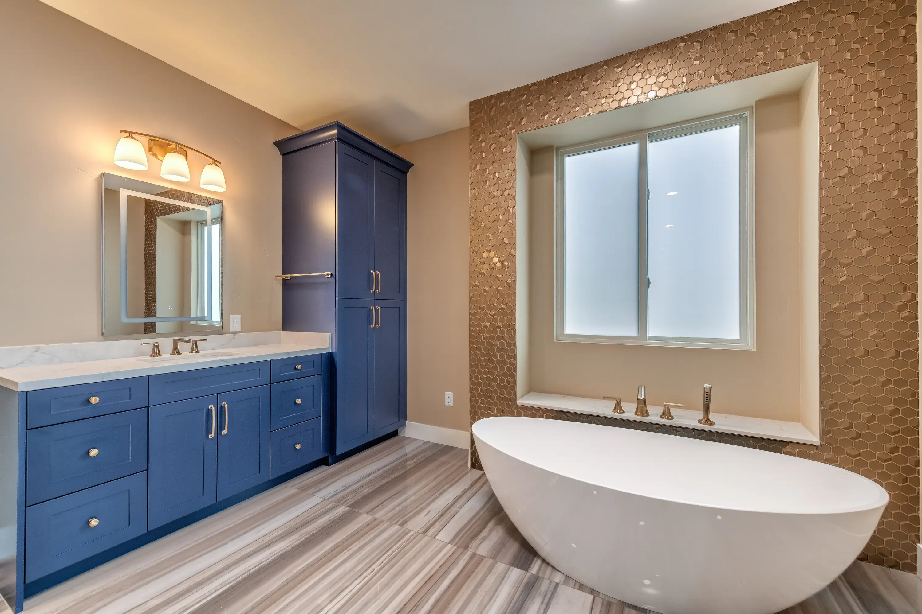 Navy vanity with marble top, freestanding tub, hexagonal tile wall, and luxury vinyl flooring