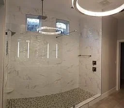 Walk-in shower with marble tile walls, frameless glass door, and recessed lighting in renovated bathroom