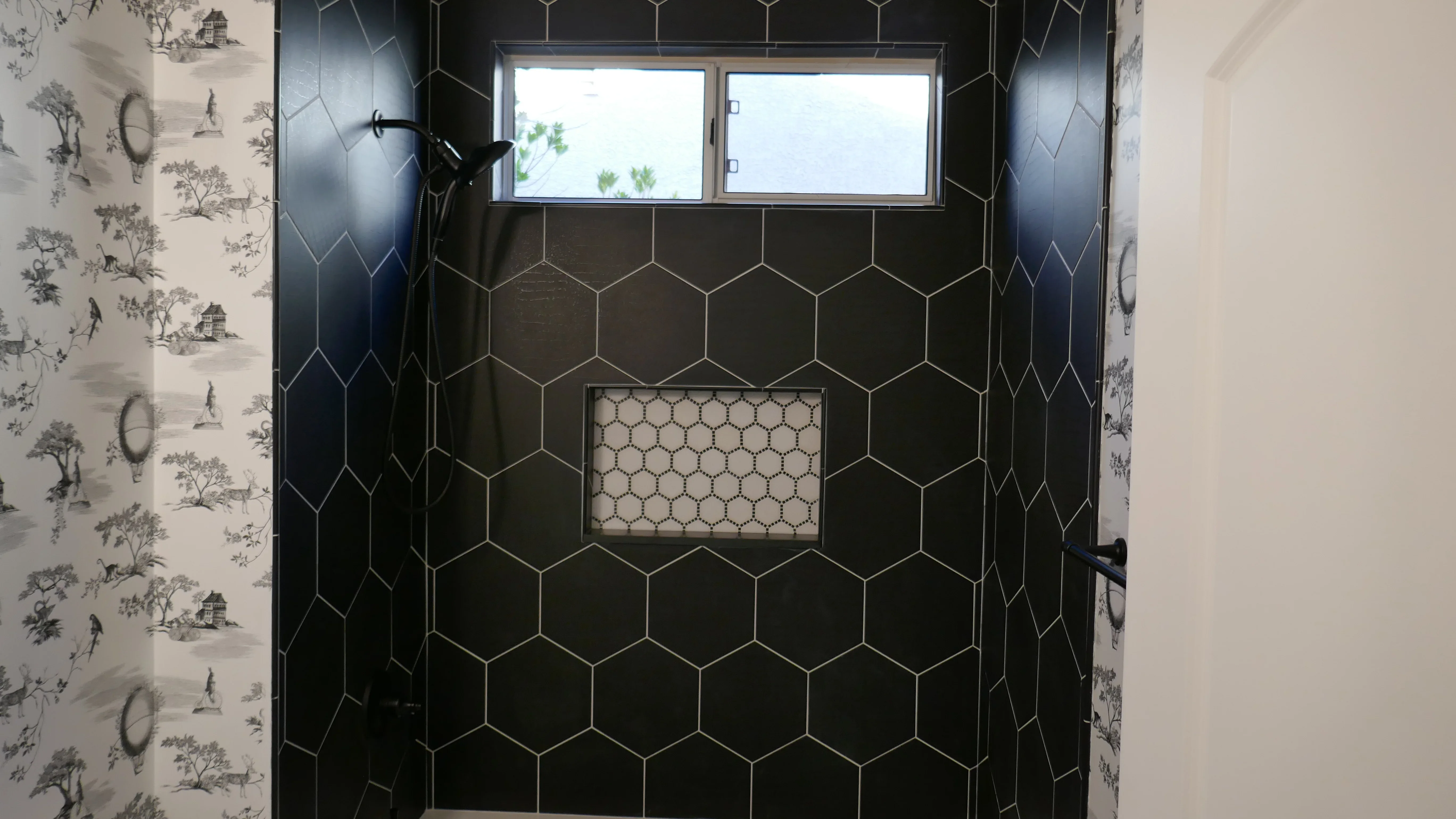 Black hexagonal tile shower enclosure with grout lines, transom windows, and recessed niche