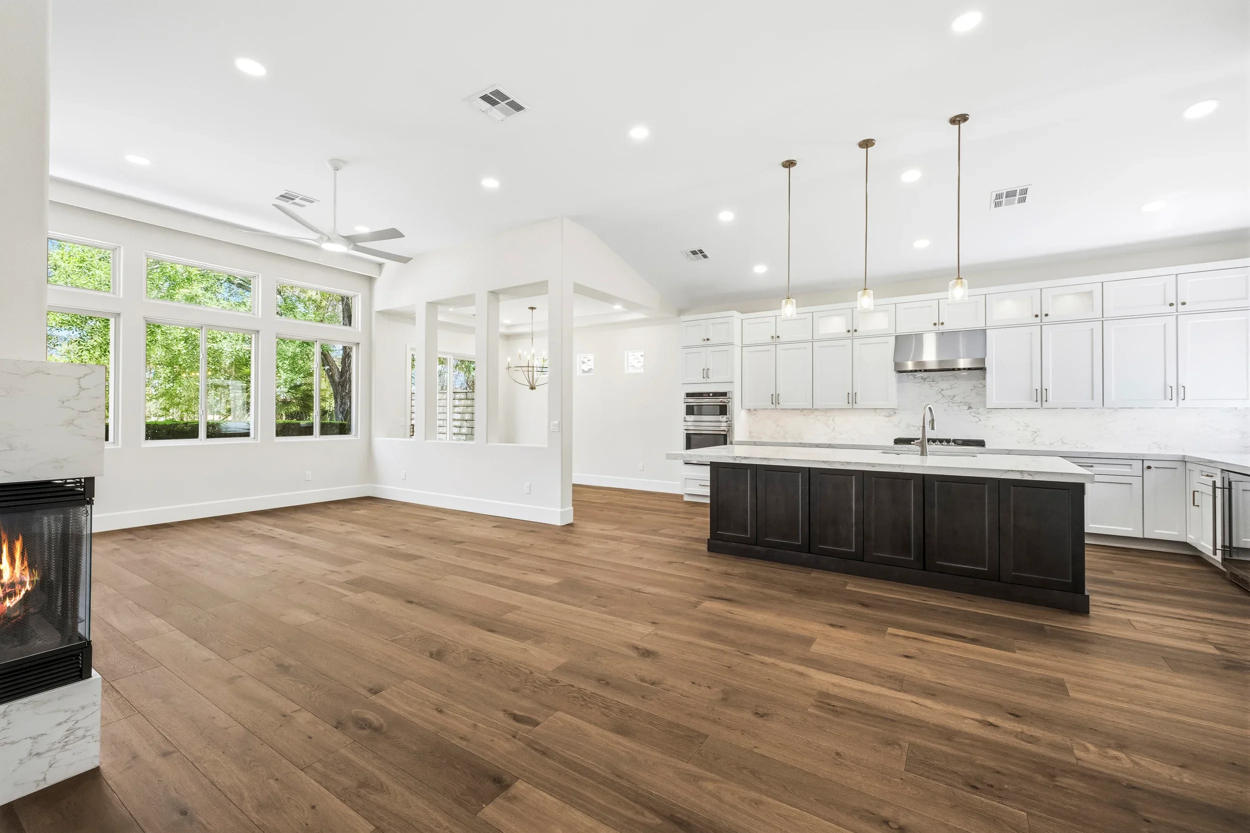 Open concept kitchen with white cabinets, dark island, hardwood floors, and marble backsplash