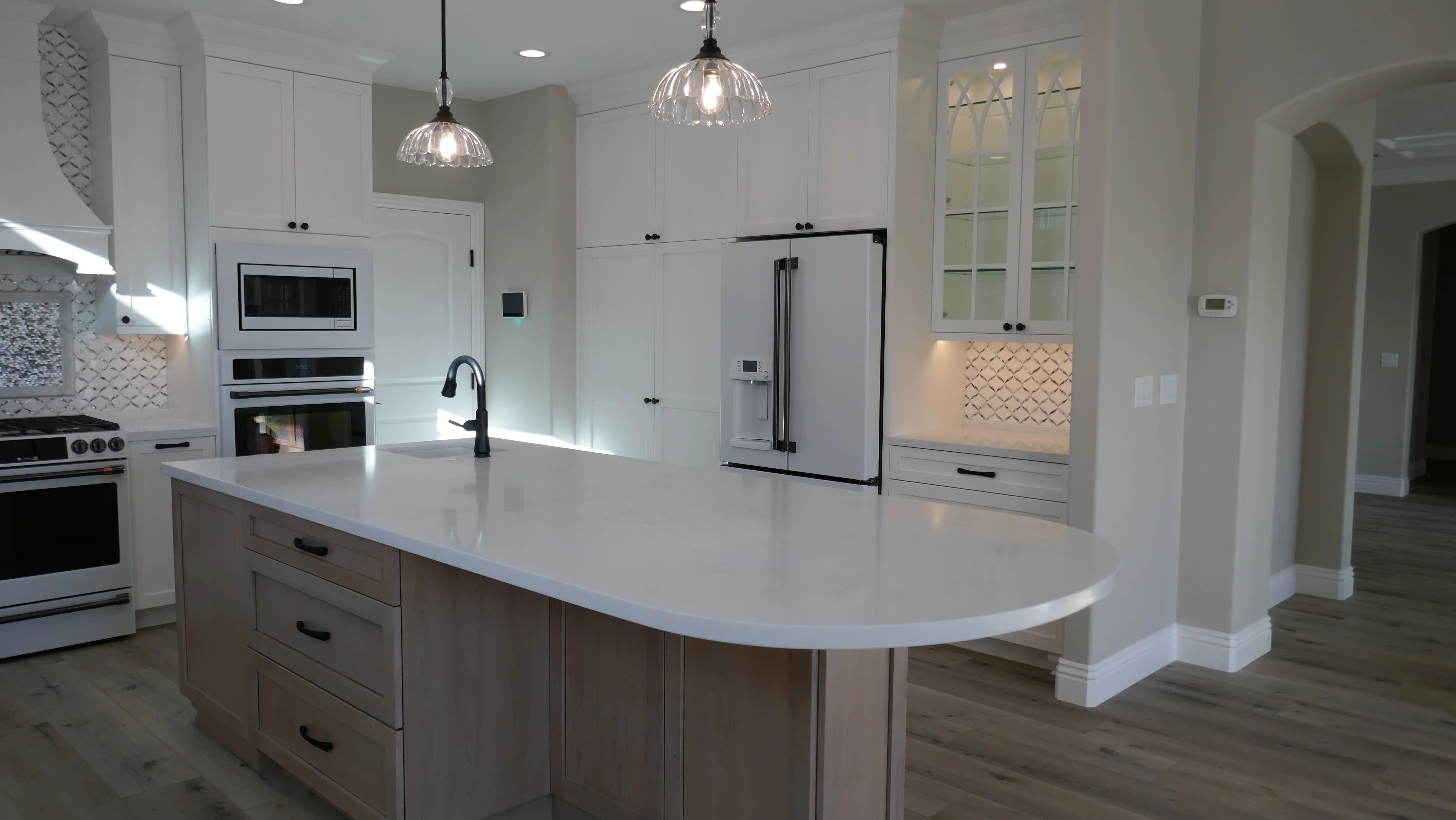 Modern kitchen with white cabinets, curved quartz island, stainless steel appliances, and geometric tile backsplash