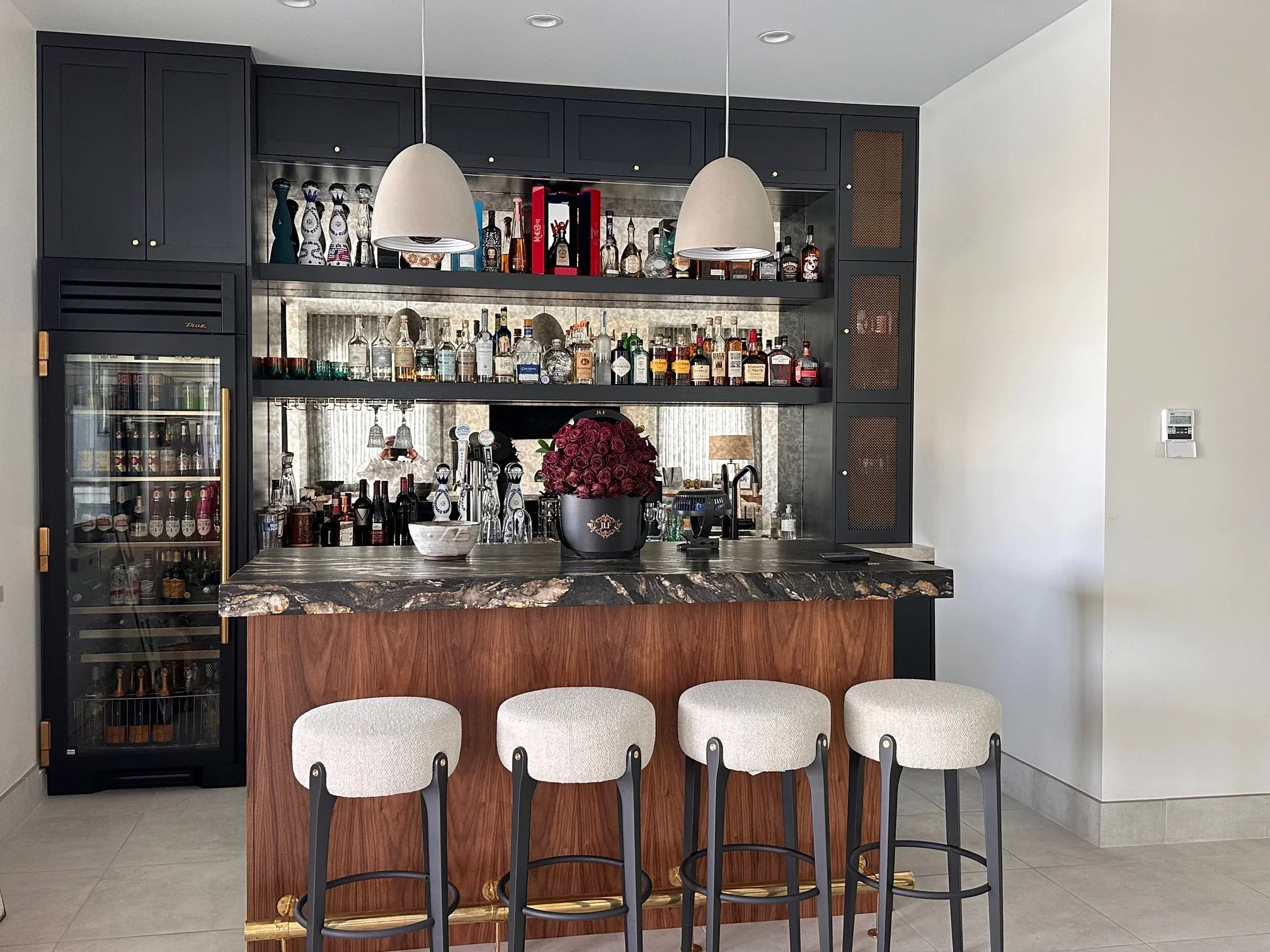 Black cabinetry bar with marble countertop, walnut front, glass shelves, and four upholstered stools
