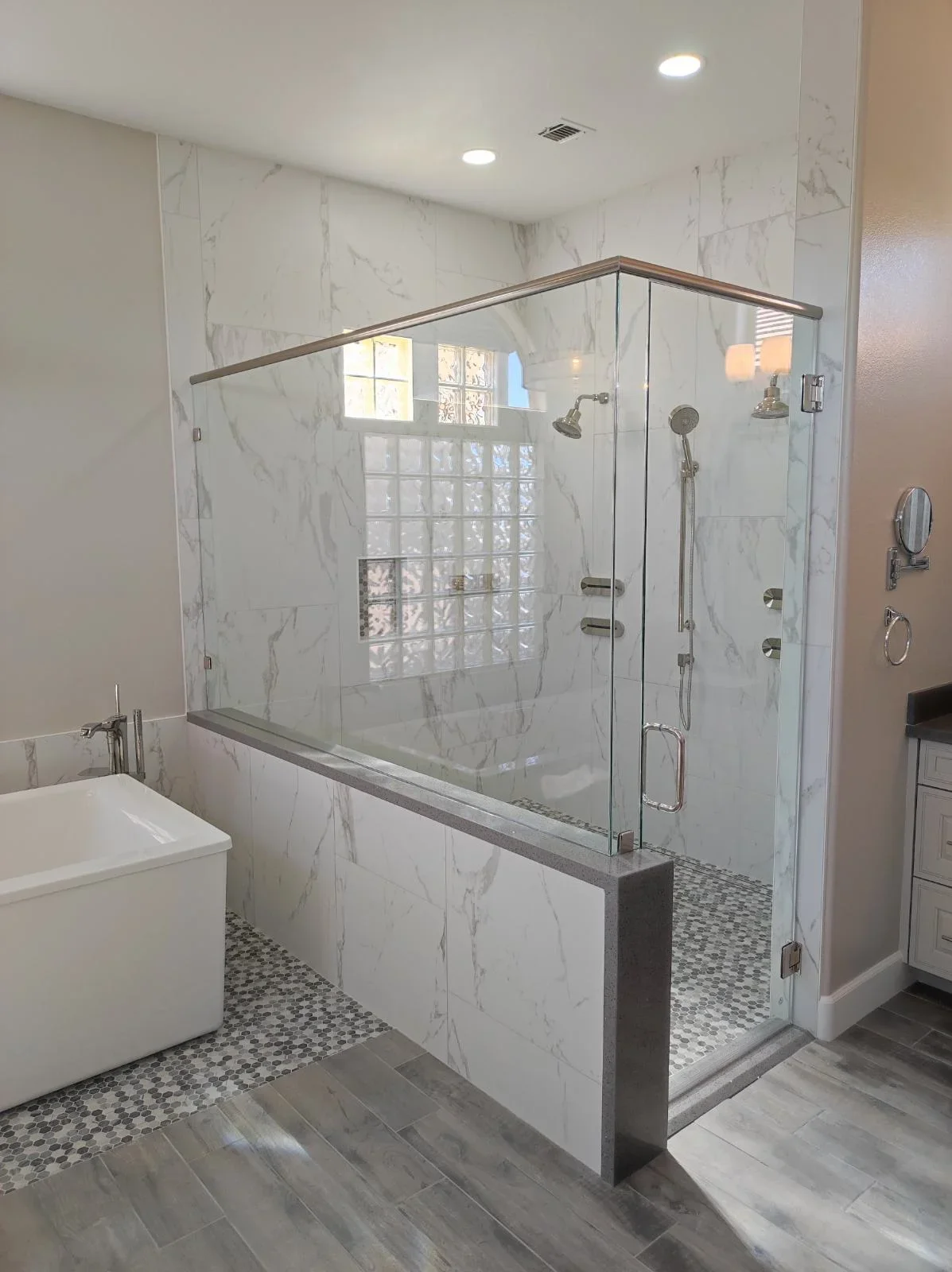 Marble bathroom with frameless glass shower enclosure and mosaic tile flooring