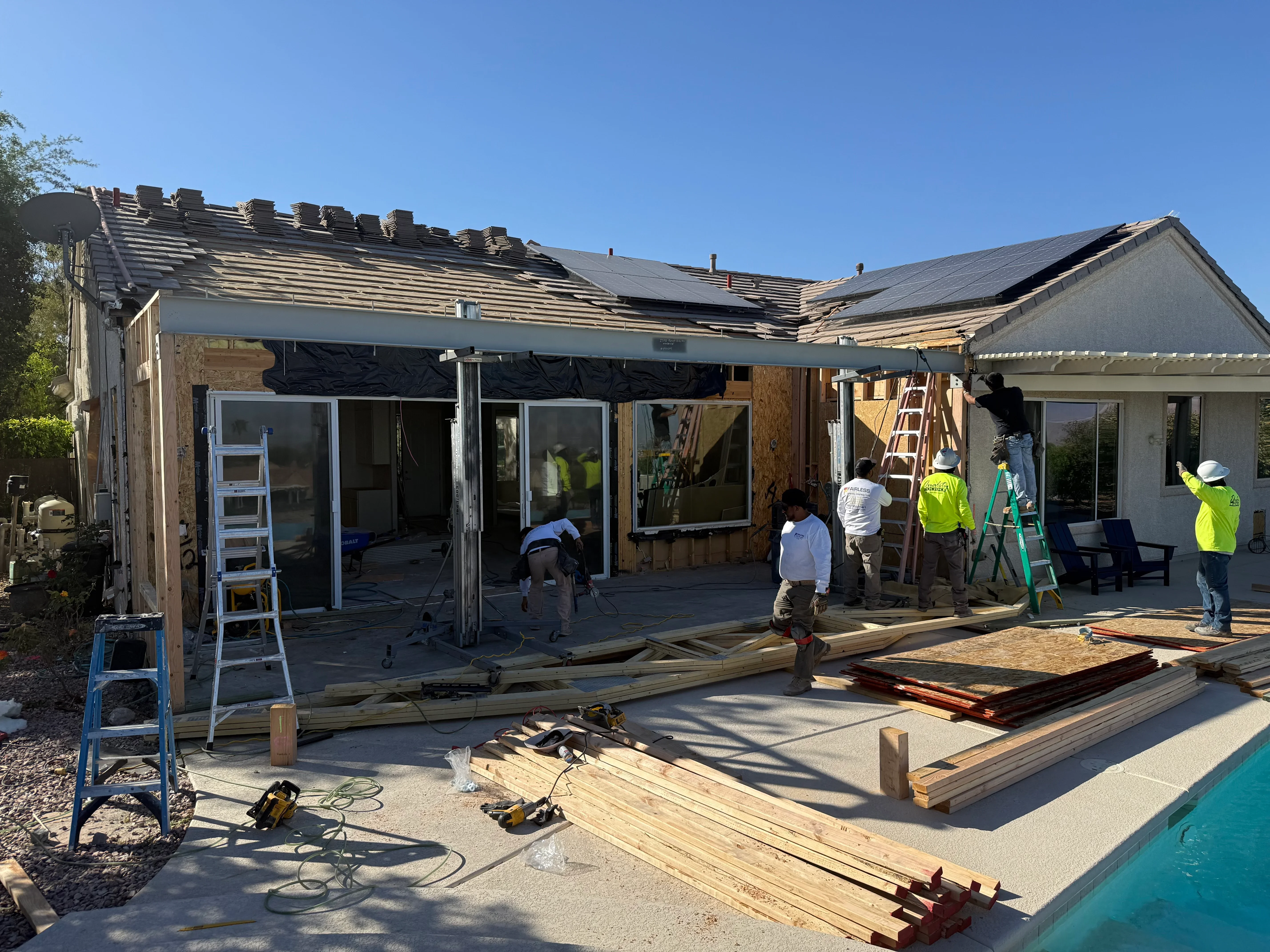 Residential addition under construction with new roof framing, sliding glass doors, and concrete patio work