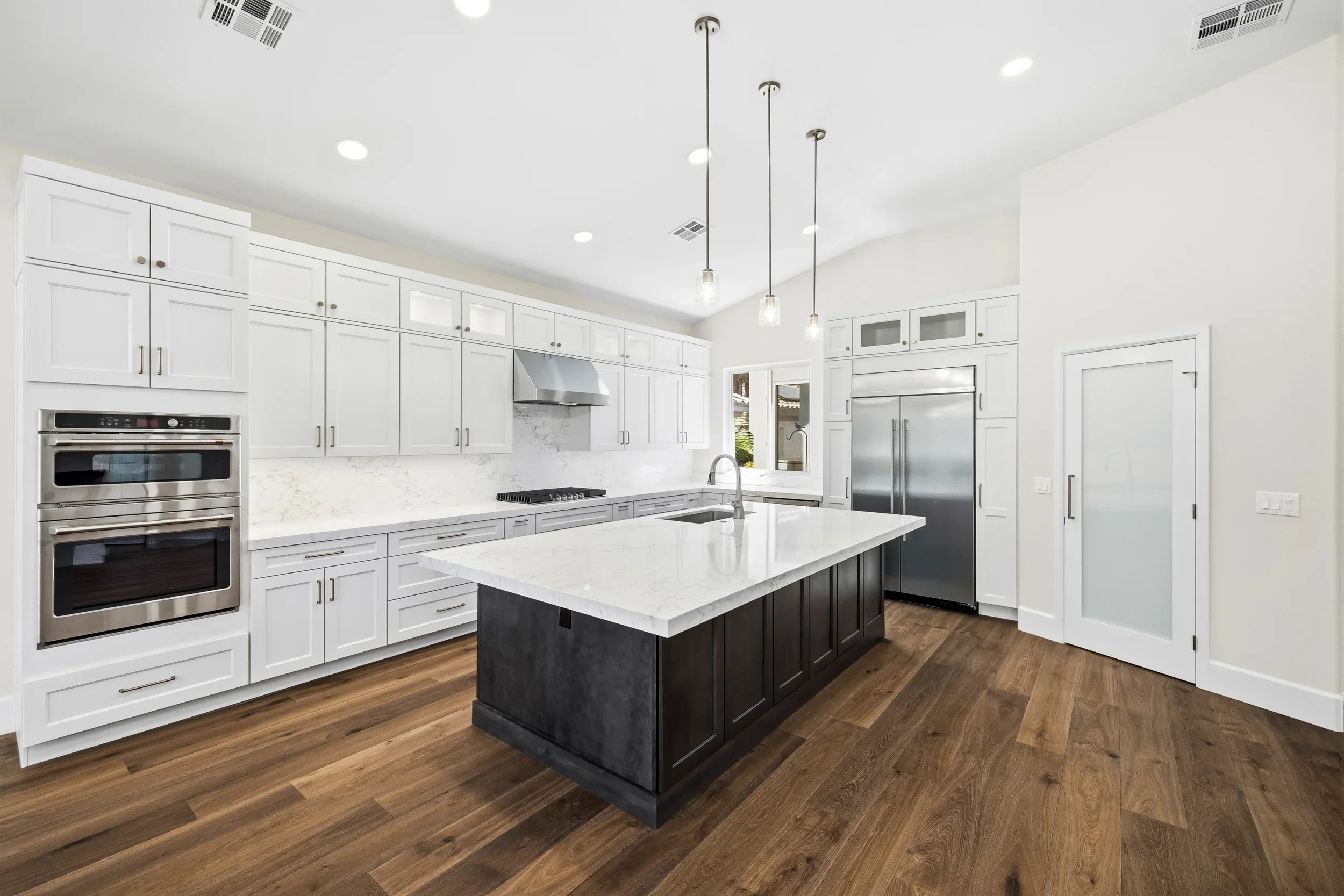Modern kitchen with white cabinetry, dark island, quartz counters, stainless appliances, and hardwood floors