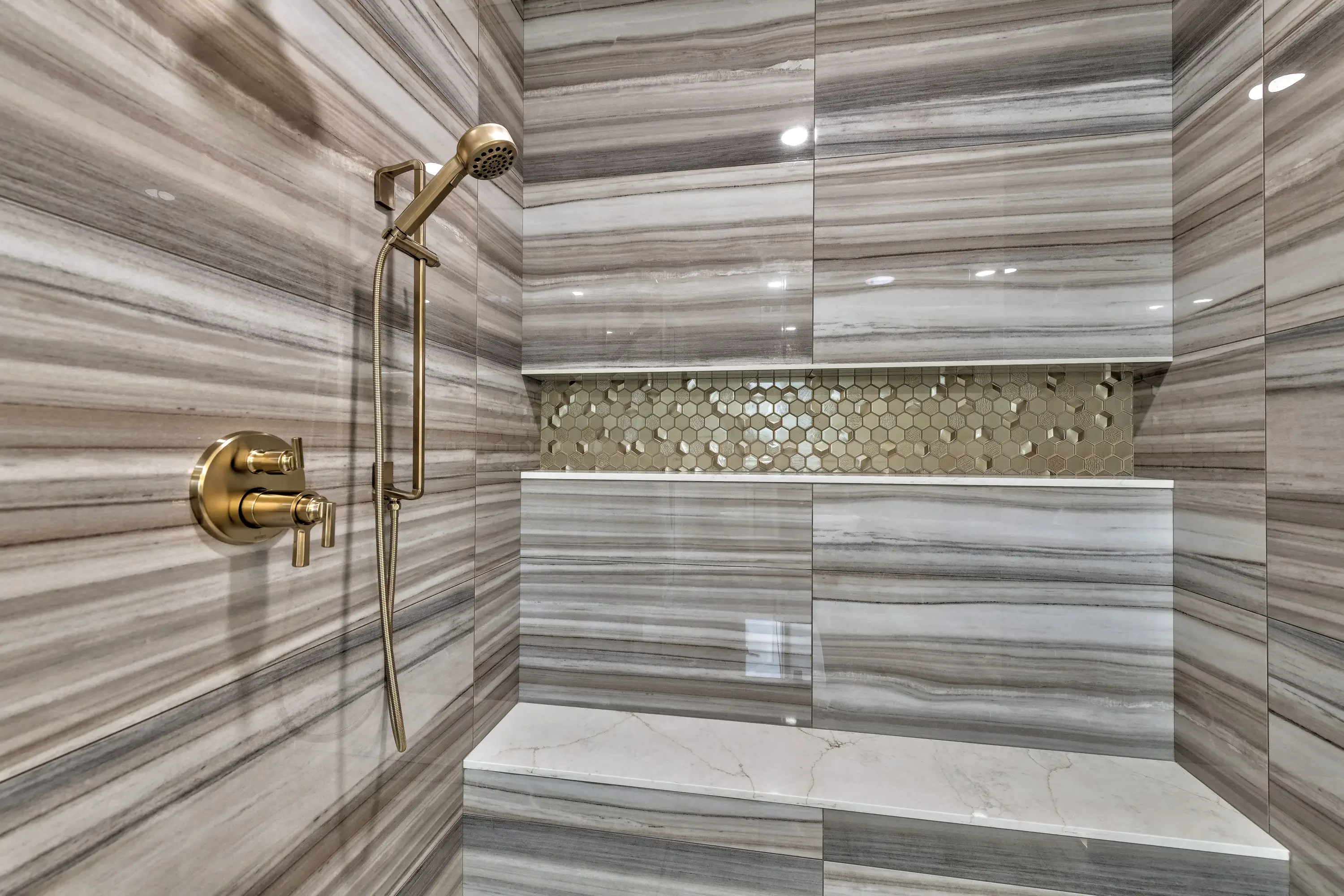 Luxury bathroom with gray striped tile walls, marble bench, hexagonal mosaic accent, and brass fixtures