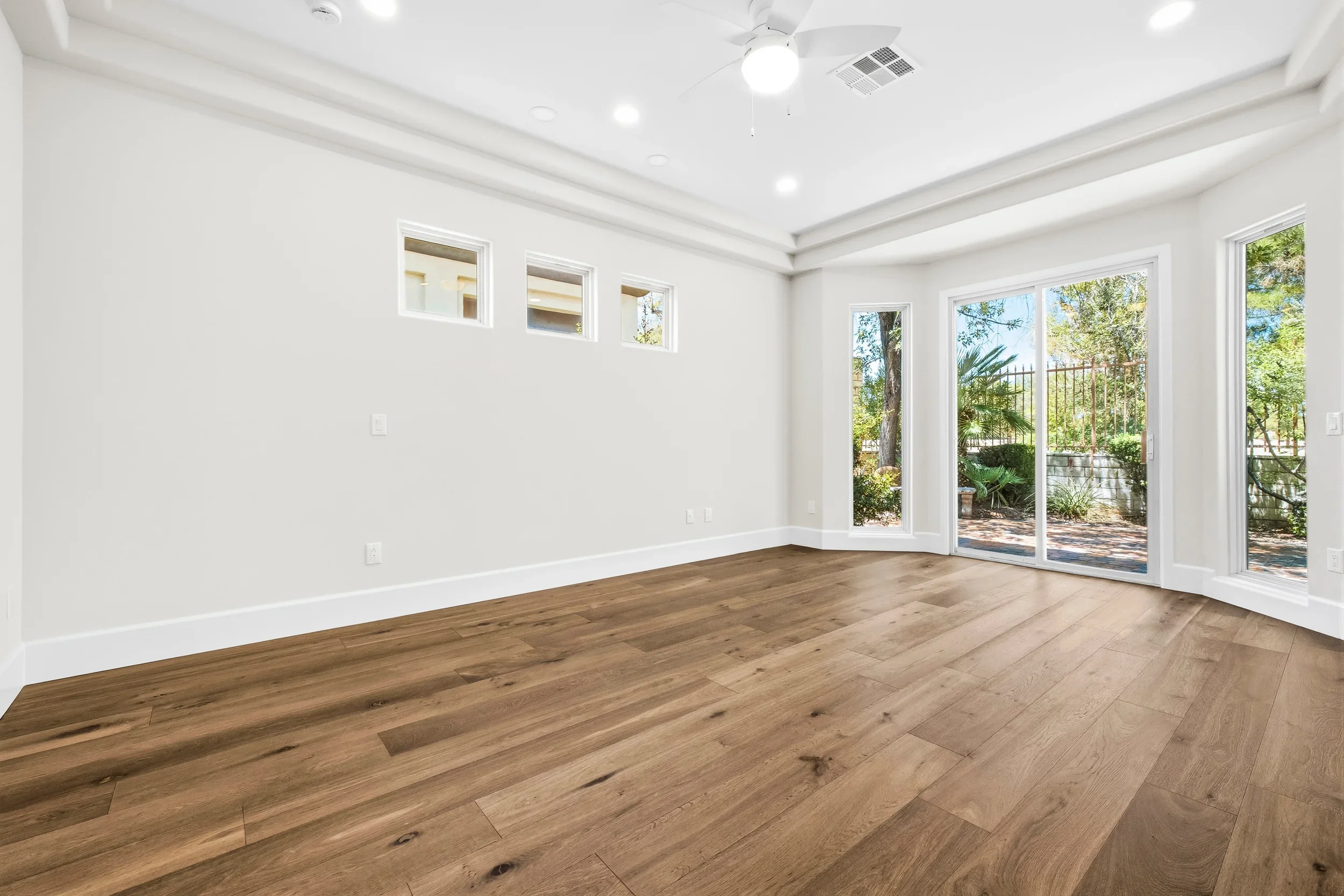 Spacious room with hardwood floors, white walls, recessed lighting, and glass sliding doors opening to deck