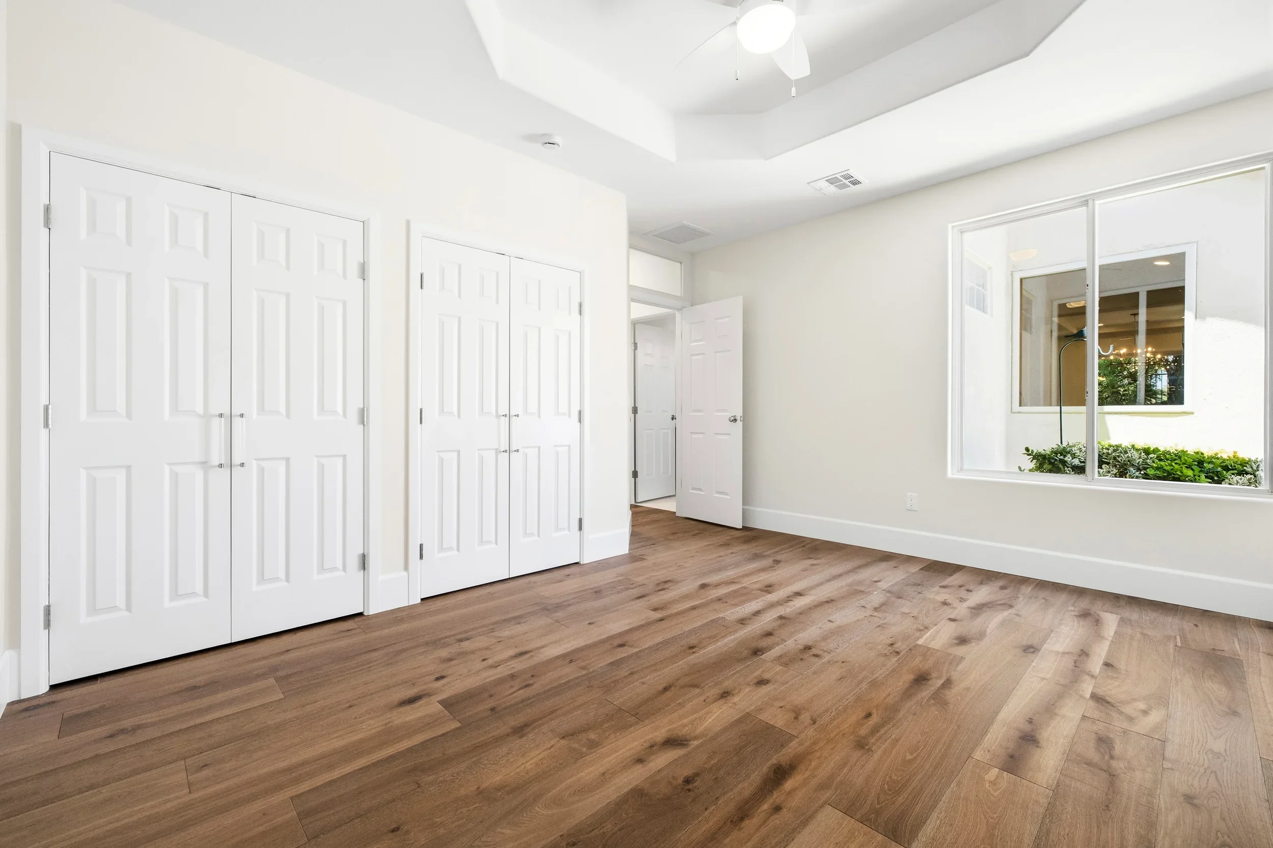 Master bedroom with white closet doors, hardwood flooring, and transom windows
