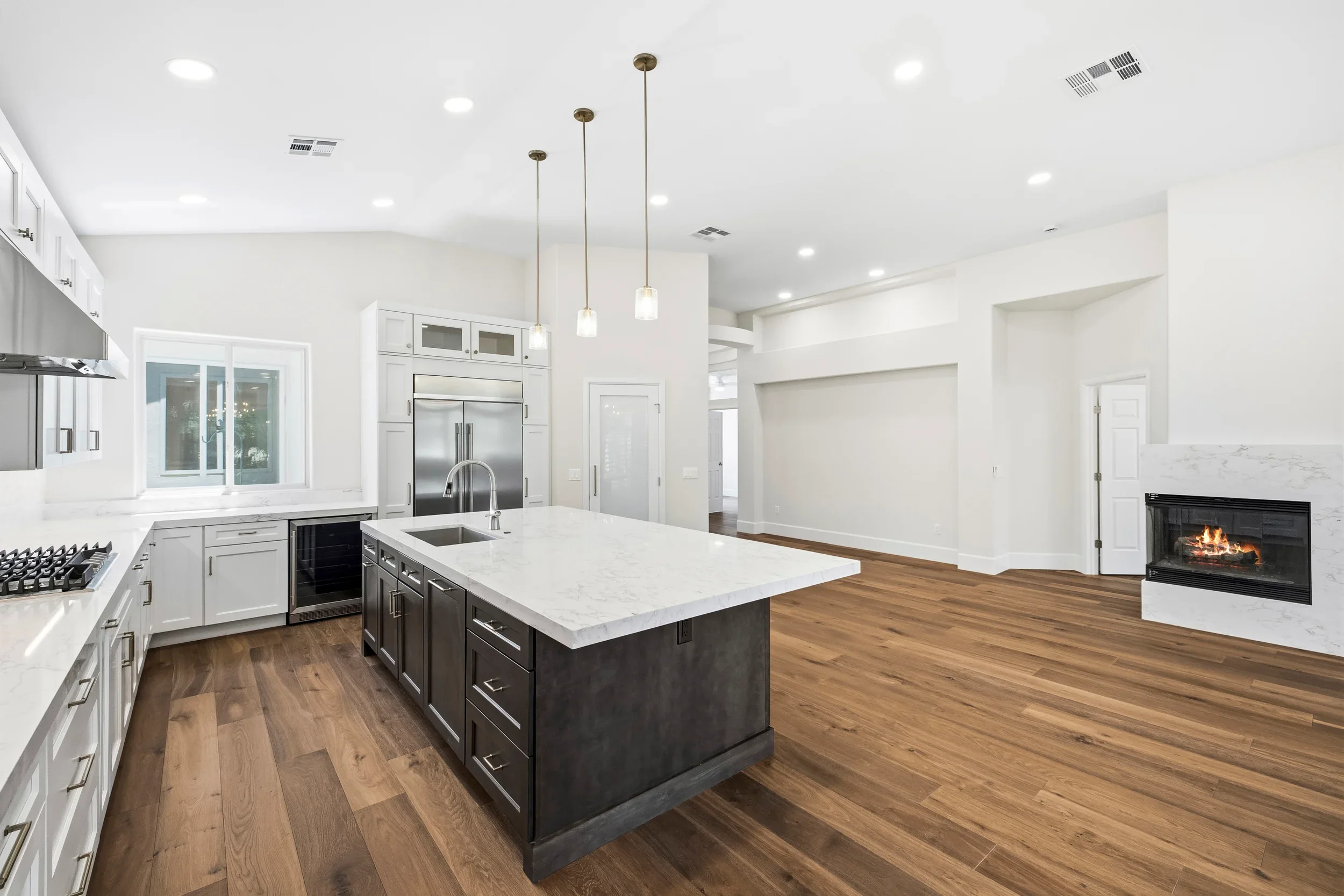 Modern kitchen with white cabinets, dark island, marble counters, stainless steel appliances, and hardwood floors