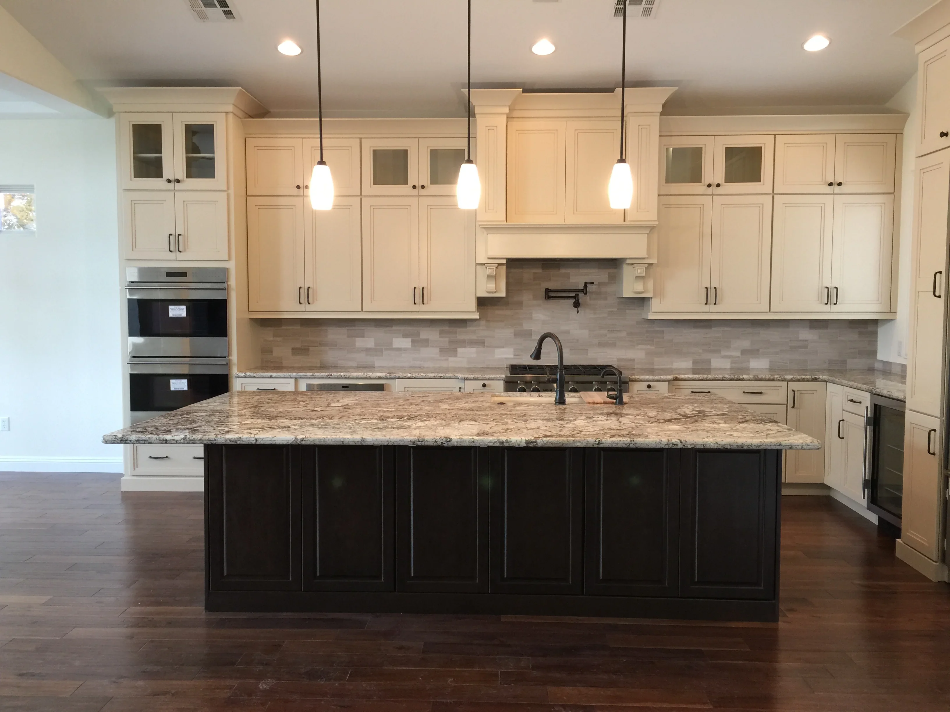 Cream and black kitchen with granite island, subway tile backsplash, and stainless steel appliances