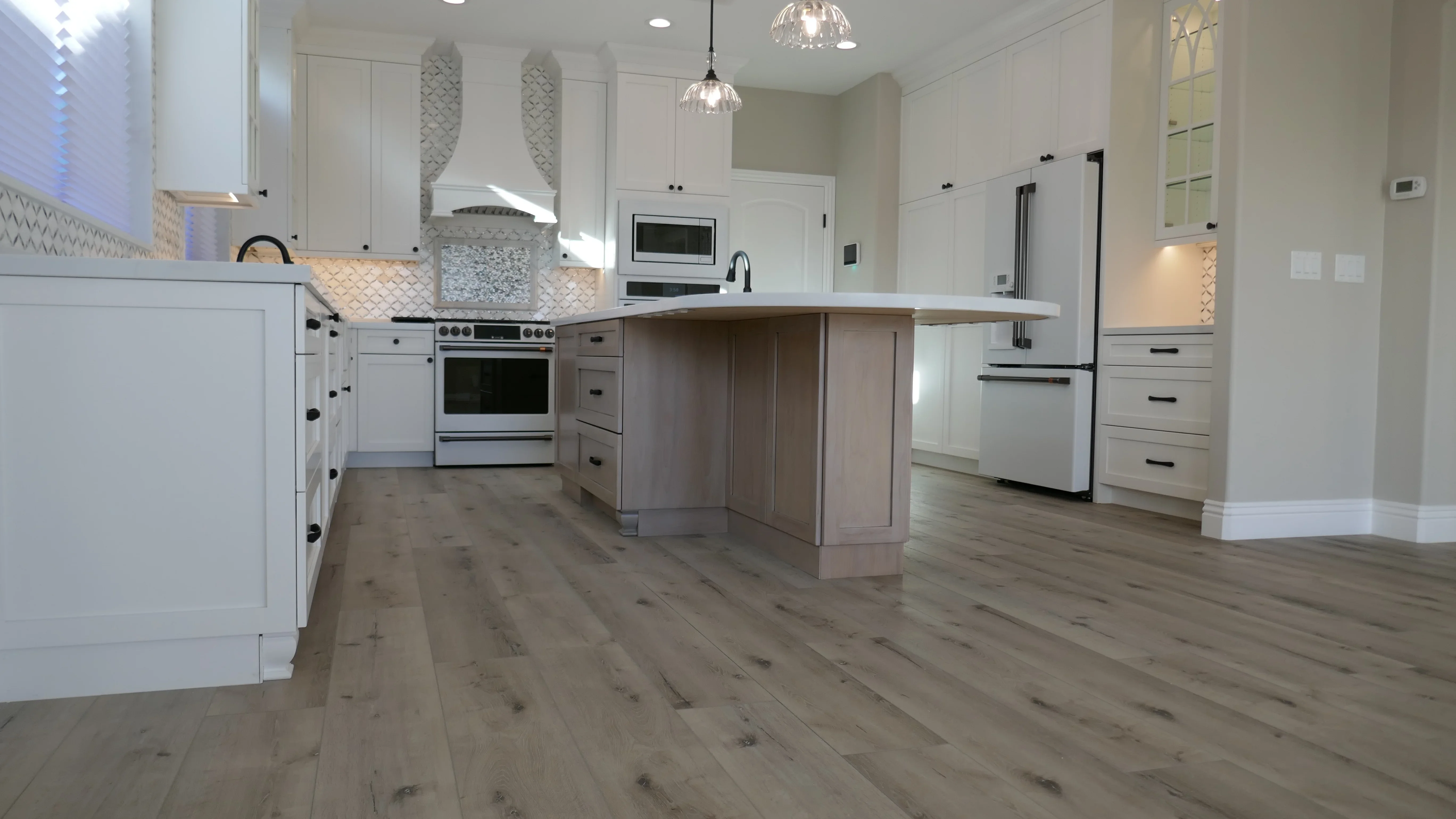 White kitchen cabinets, two-tone island, geometric tile backsplash, stainless steel appliances, wood flooring