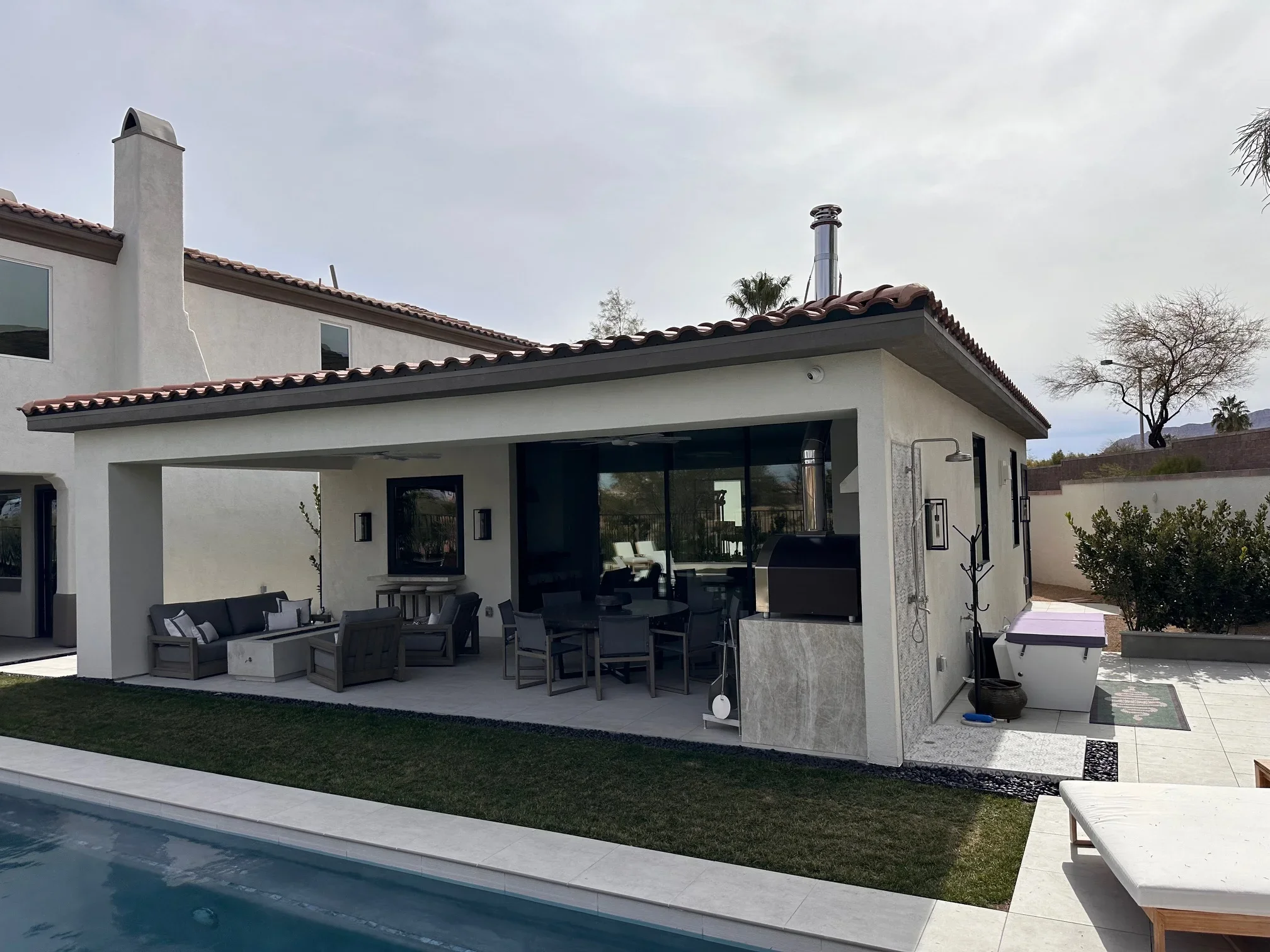 White stucco patio cover with steel beams, concrete counters, and large sliding glass doors overlooking pool
