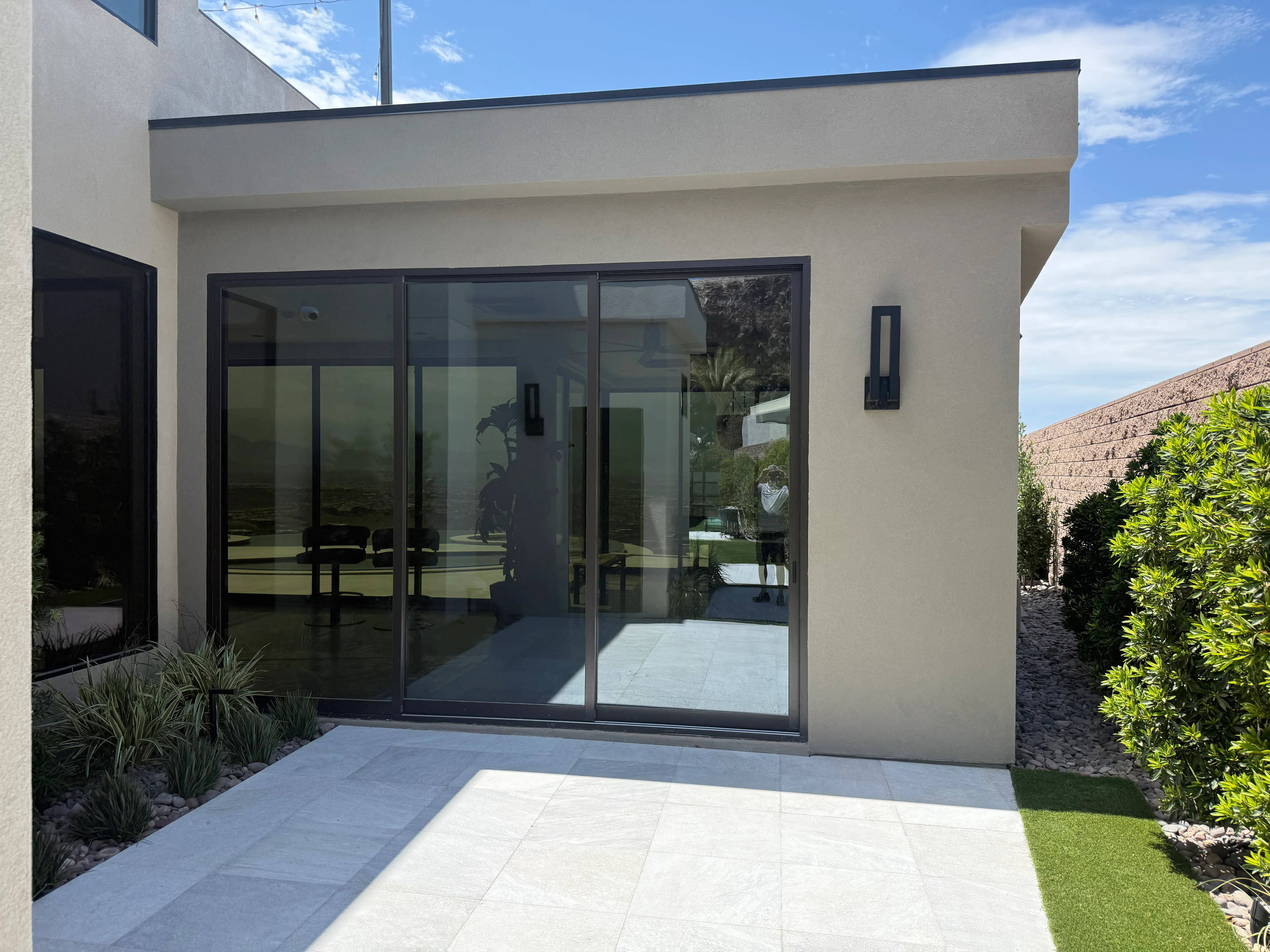 Modern stucco addition with black-framed sliding glass doors and light tile patio