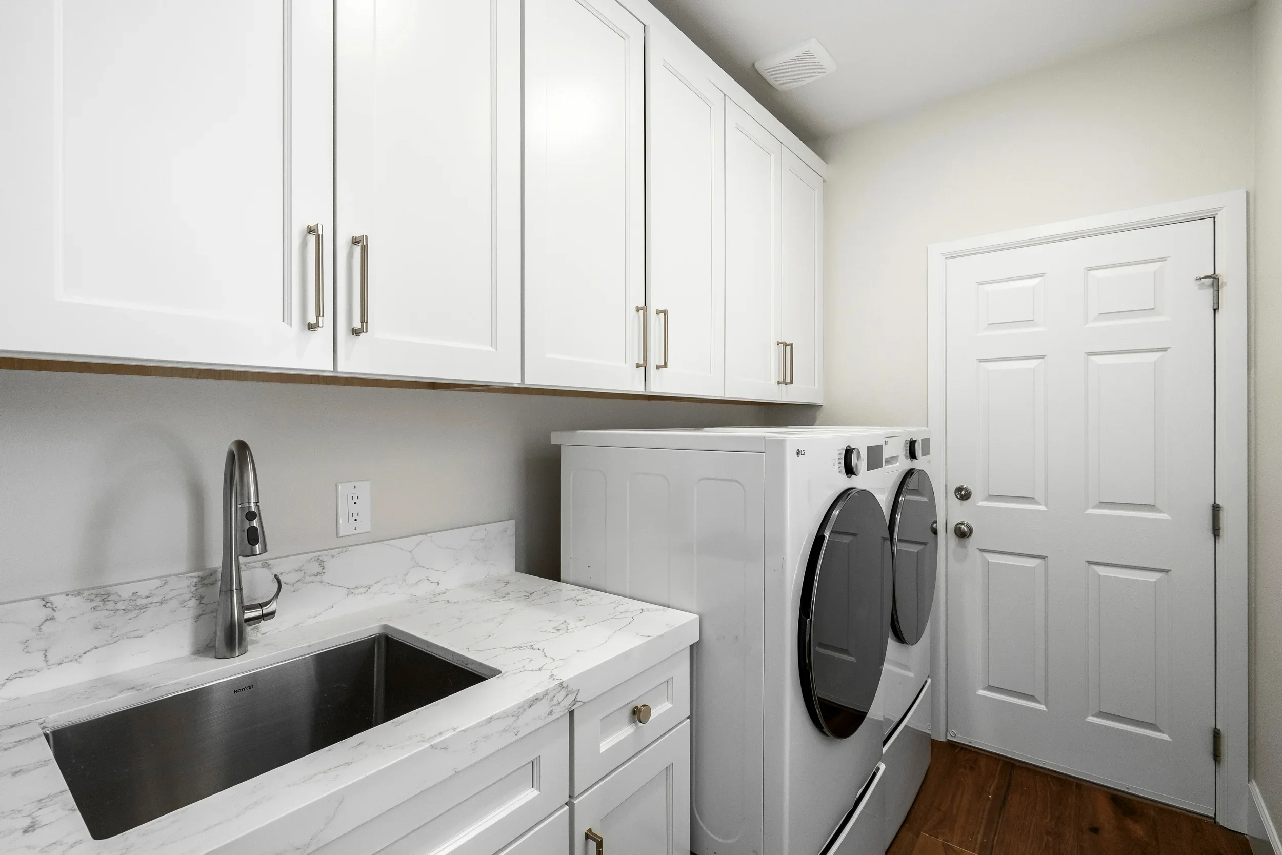 White cabinetry, marble countertop, stainless steel sink and faucet, integrated washer-dryer space