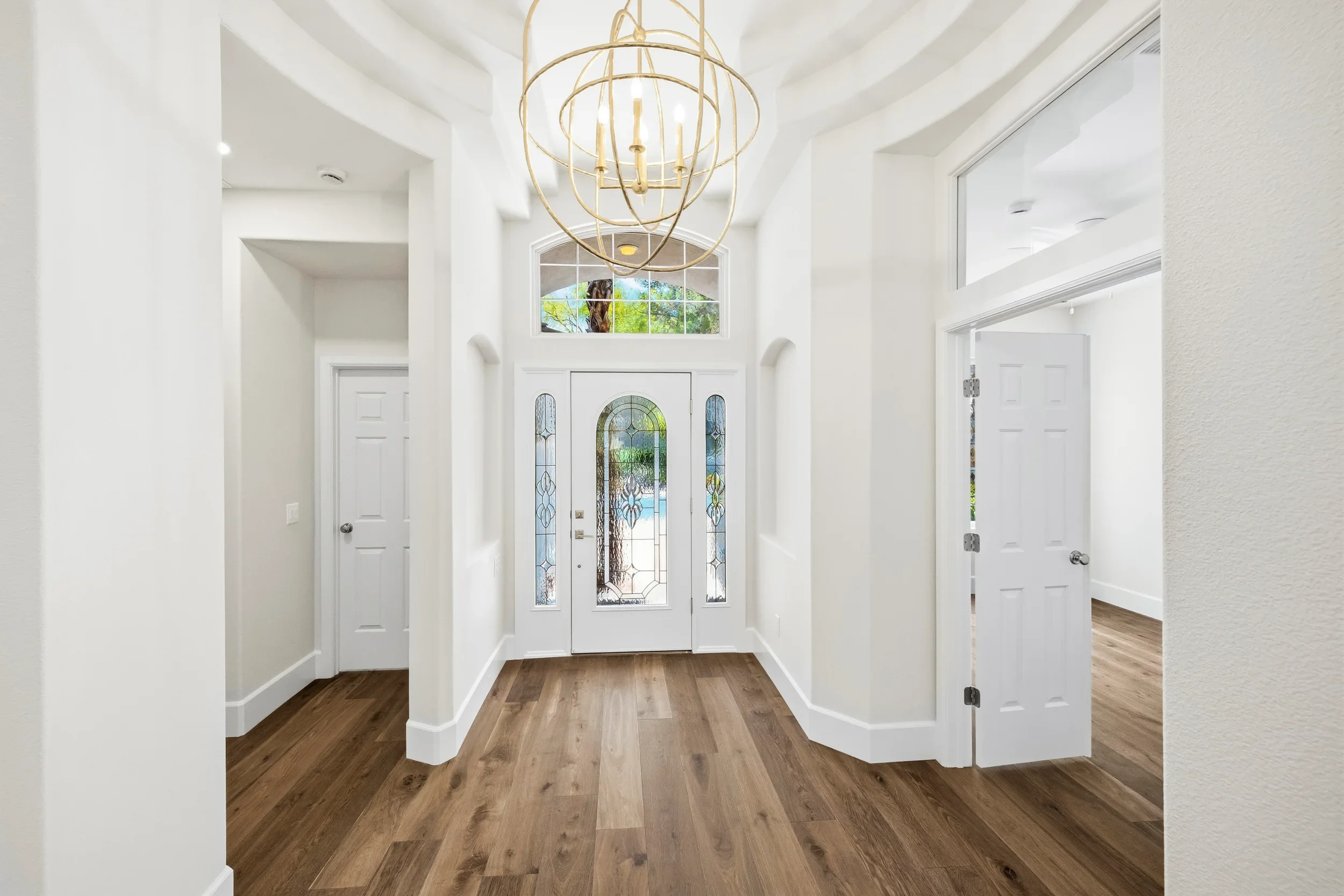 White painted foyer with arched doorways, coffered ceiling, stained glass transom windows, and wood flooring
