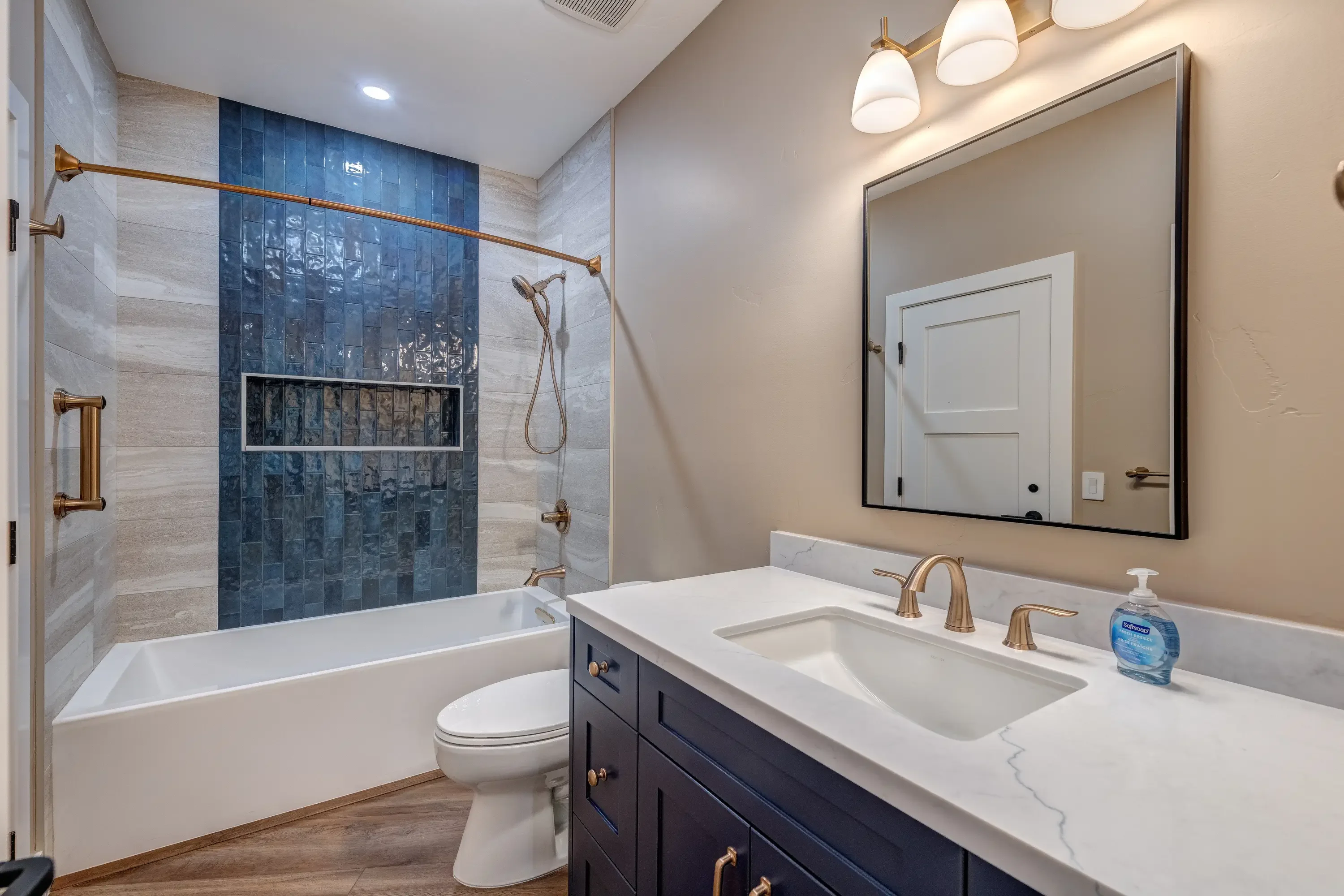 Modern bathroom with blue tile shower, white vanity, quartz countertop, and bronze fixtures