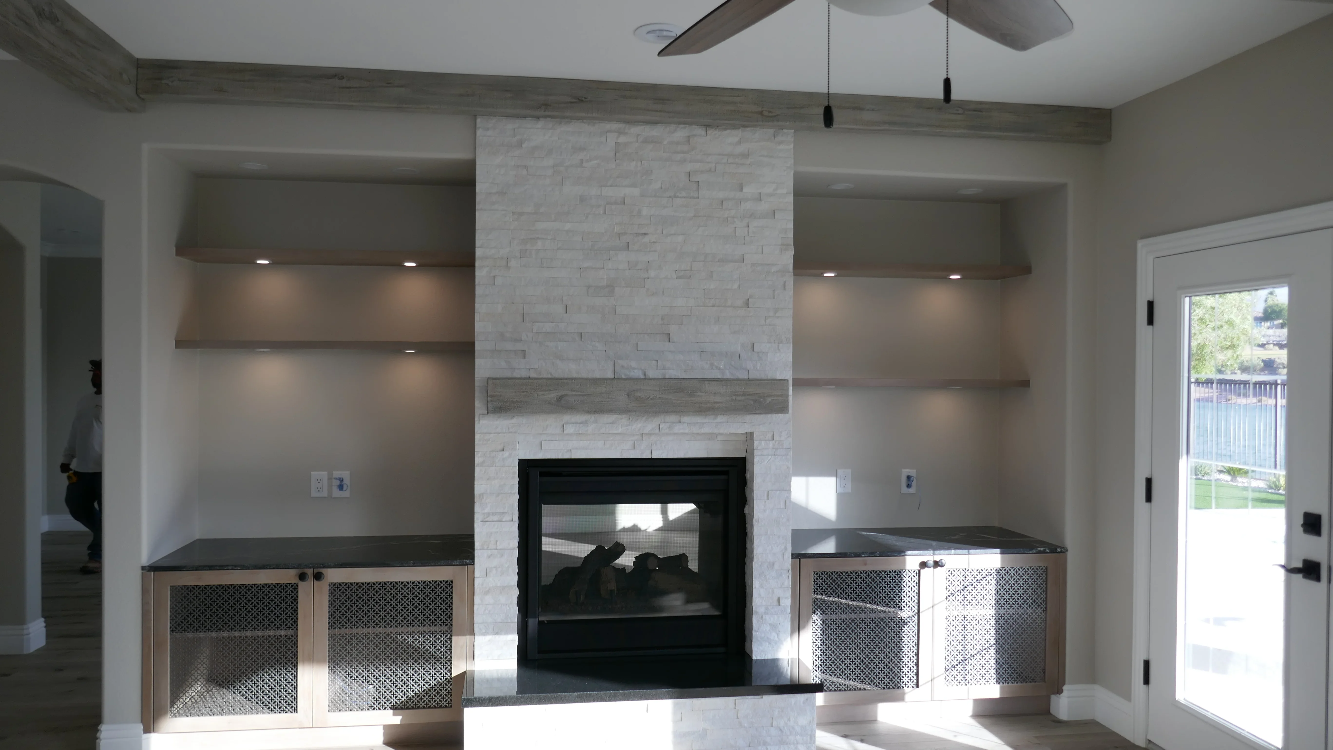 White stacked stone fireplace with black insert, wood mantel, and built-in cabinetry with mesh doors