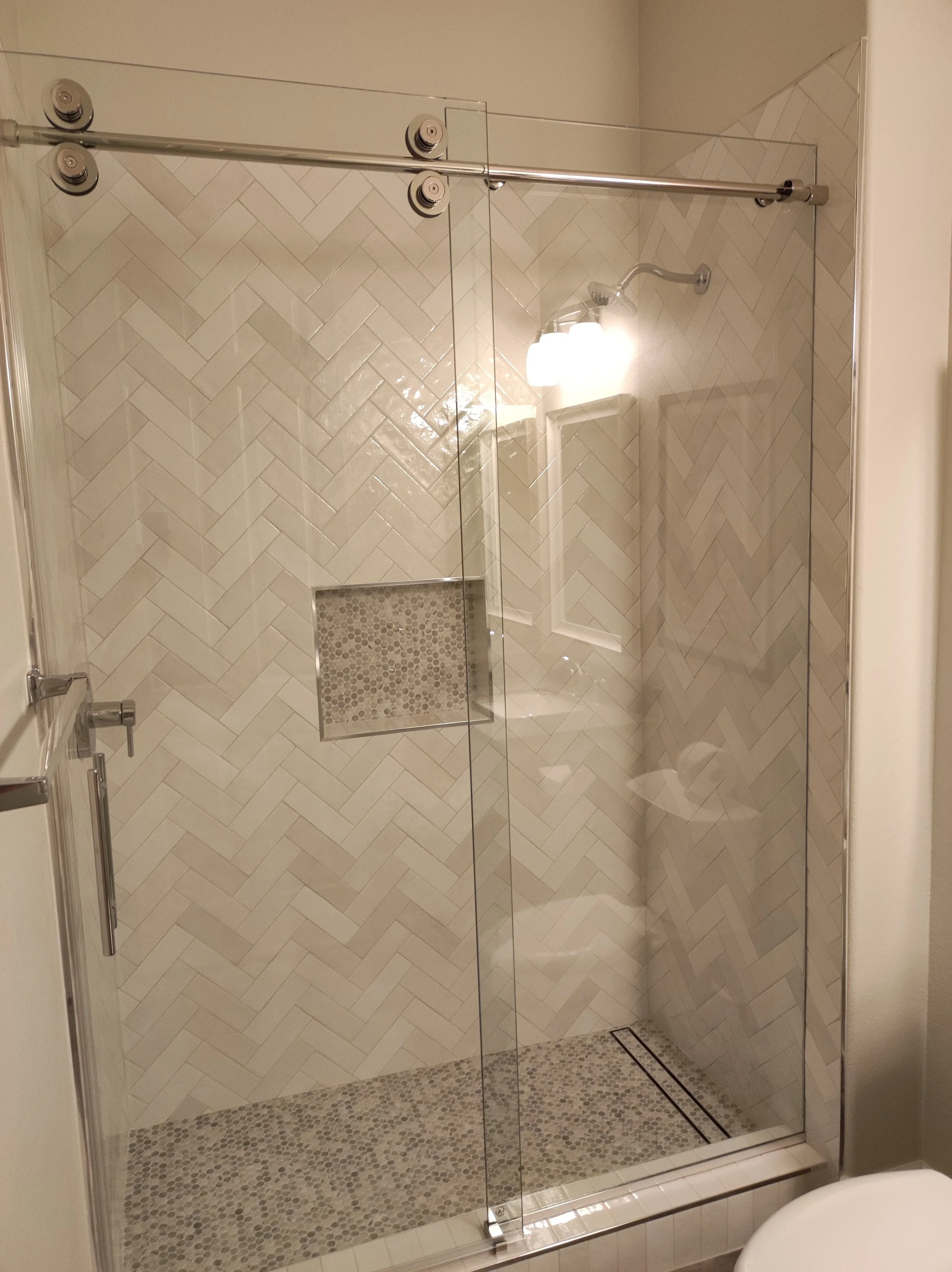 Frameless glass shower with herringbone tile walls and pebble stone floor