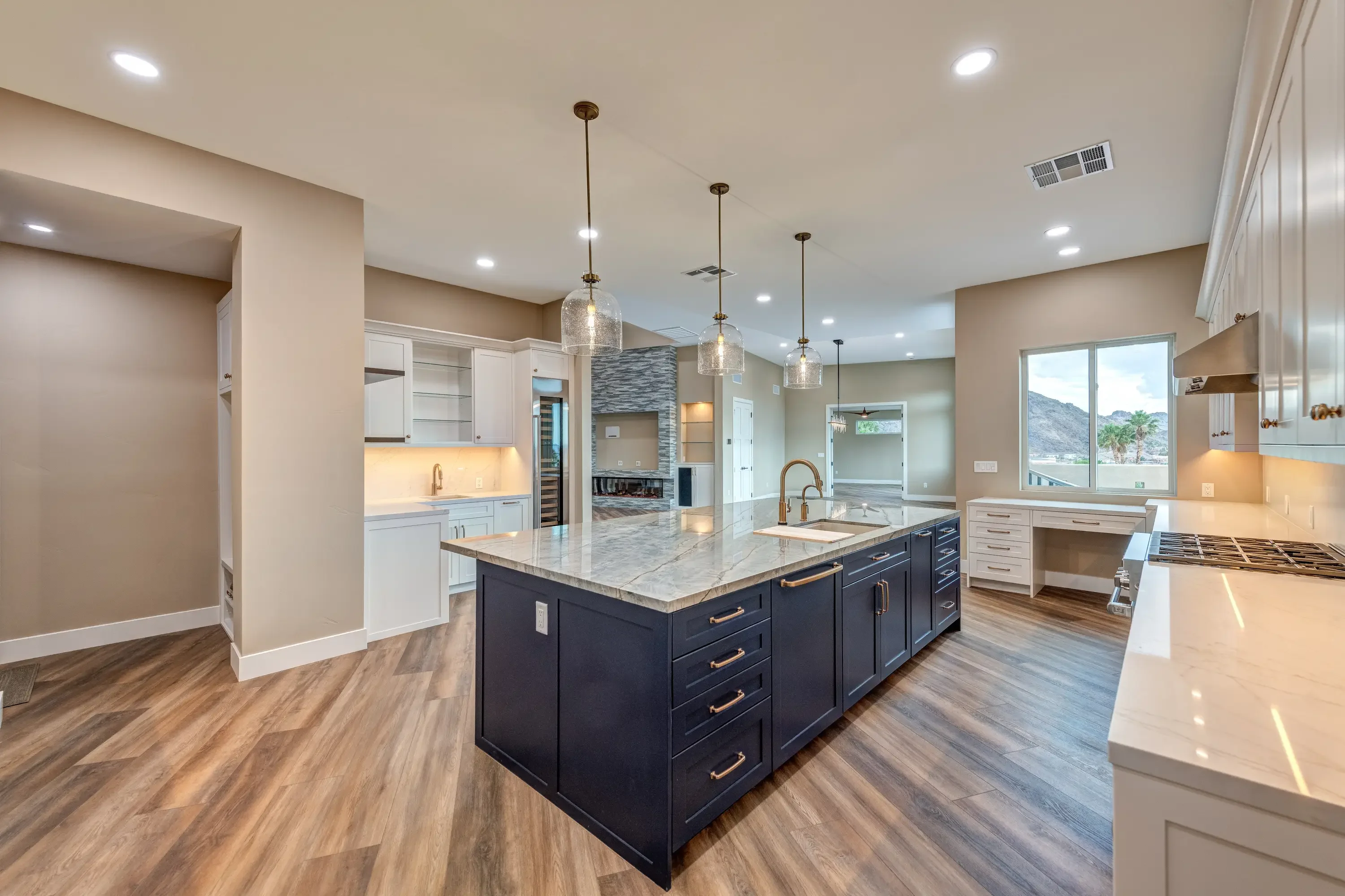 Modern kitchen with dark island, marble counters, white cabinetry, stone backsplash, and pendant lights