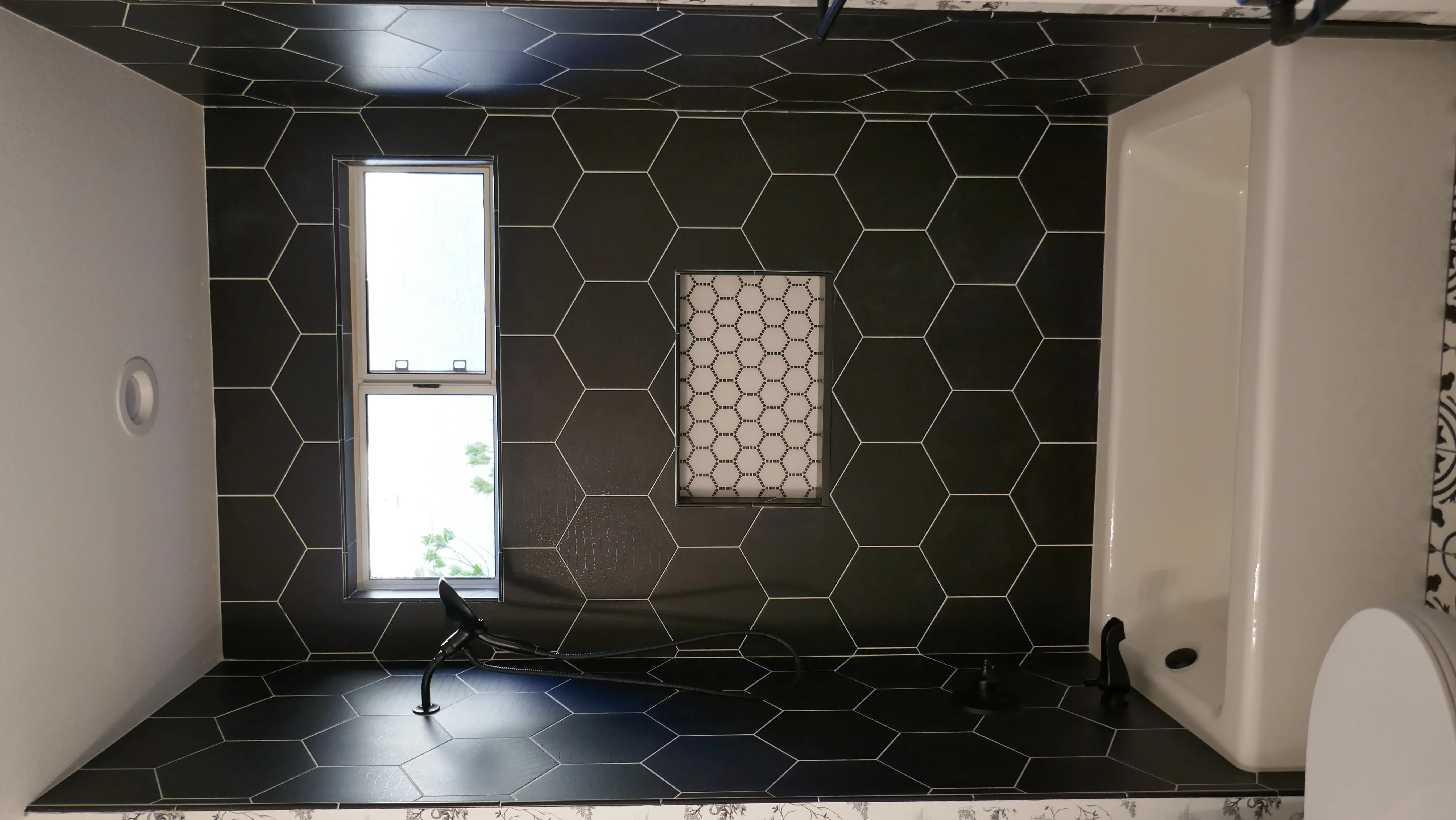 Black hexagonal tile bathroom with glass shower enclosure and white fixtures