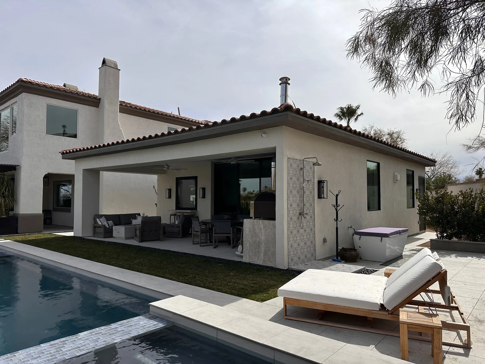 Modern stucco home addition with covered patio, black-framed glass doors, and pool deck