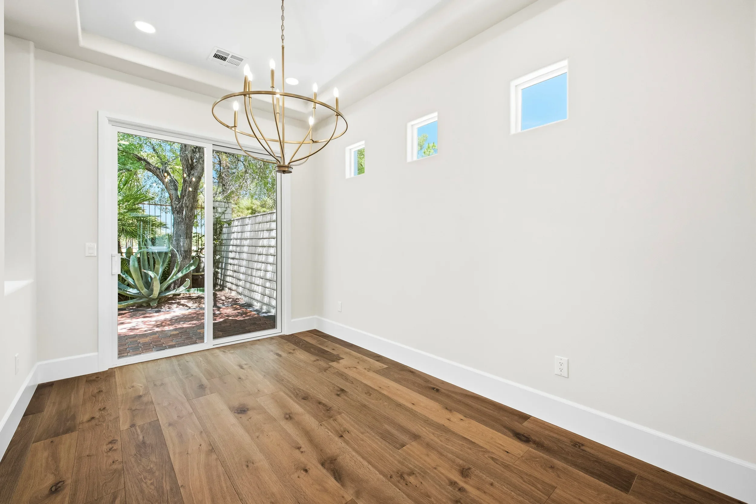 Modern room with hardwood floors, white walls, French doors, and brass pendant lighting