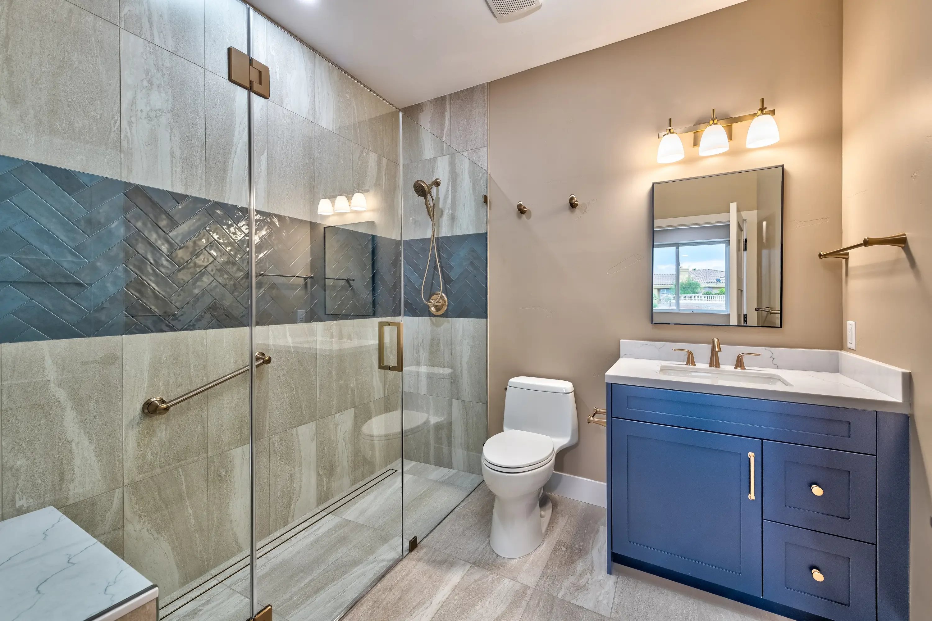 Master bathroom with glass shower enclosure, herringbone tile, navy vanity, and white quartz countertop