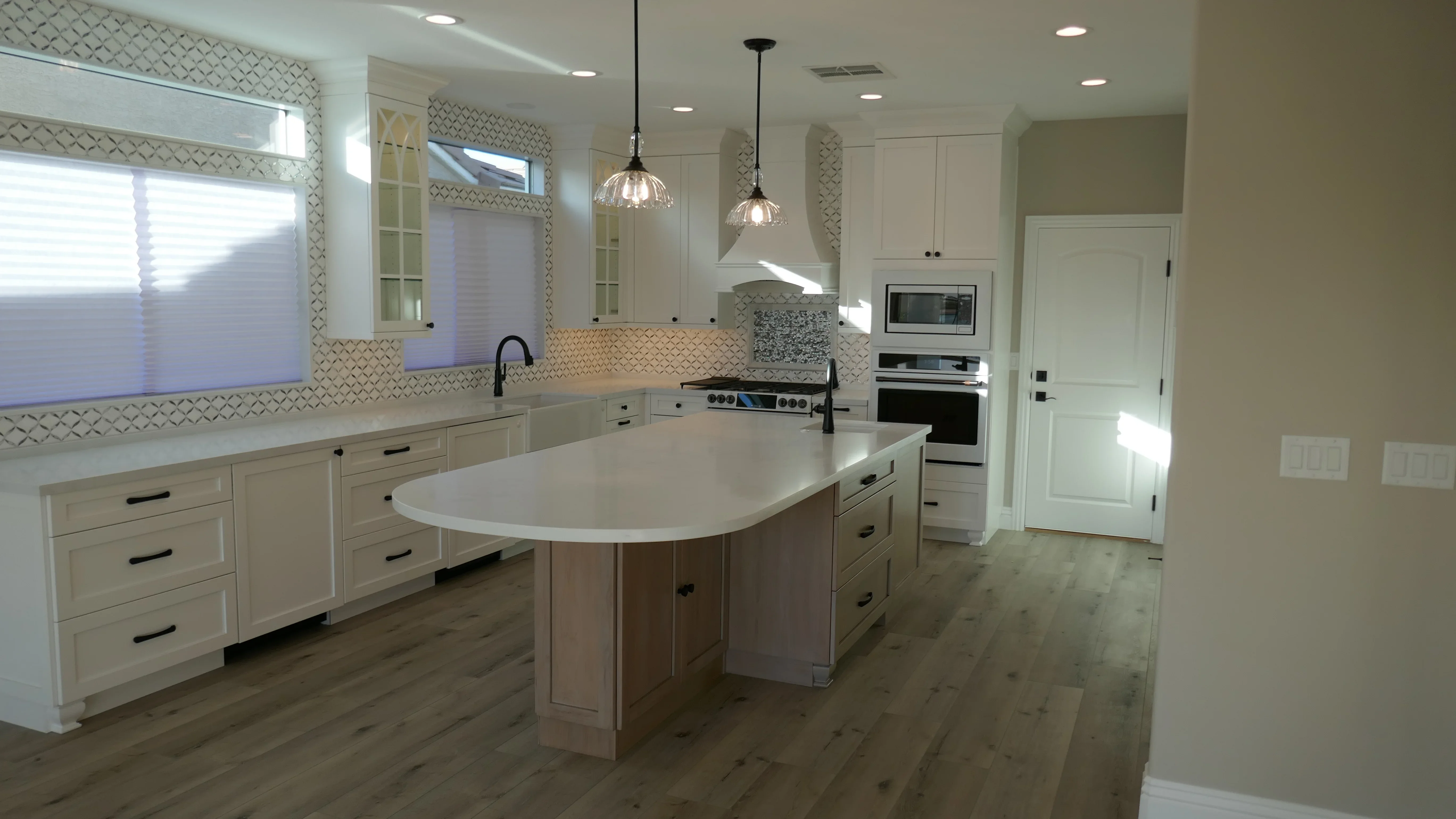 White kitchen cabinetry, quartz countertops, geometric tile backsplash, stainless steel appliances, pendant lights, hardwood floor