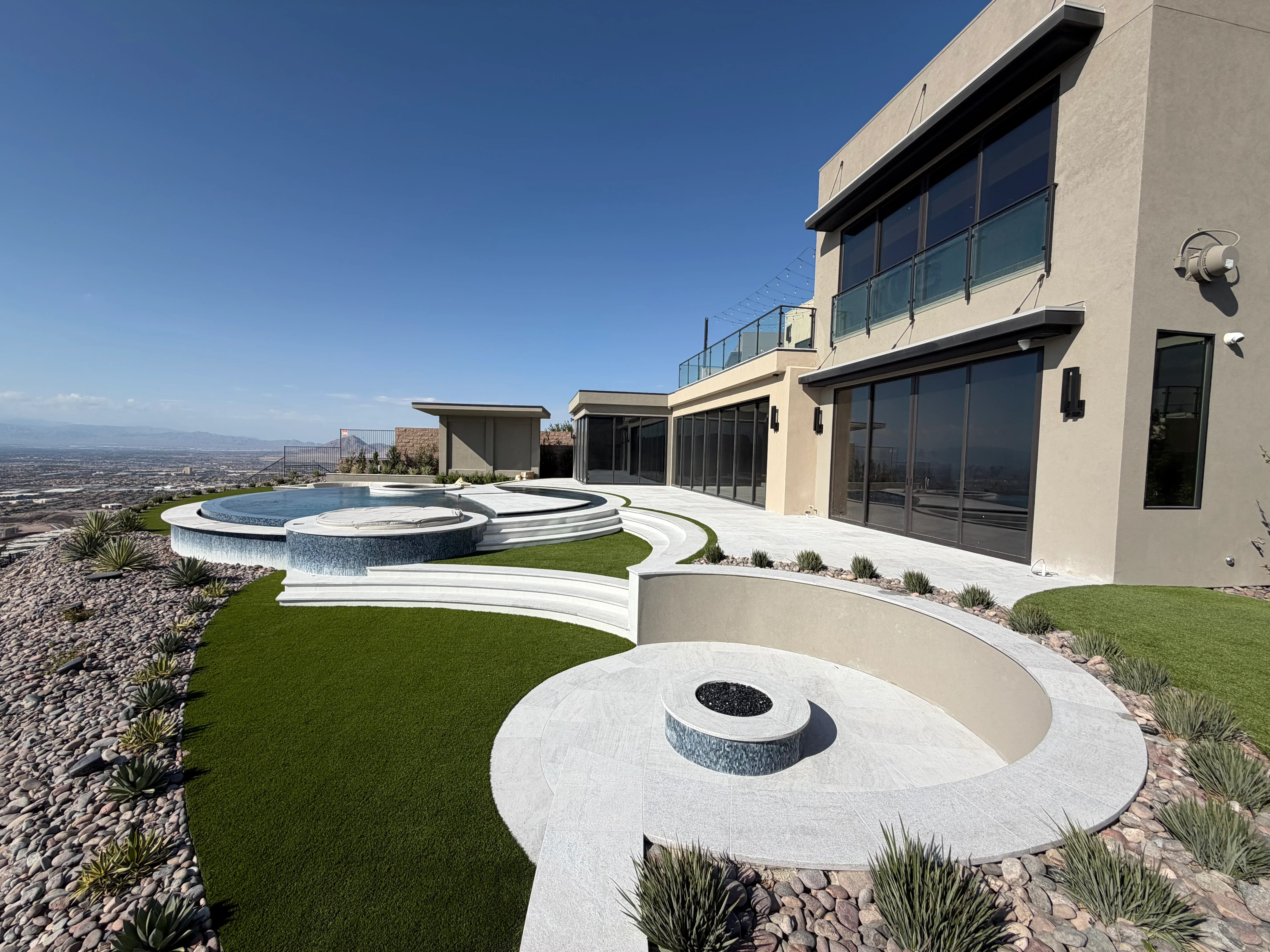 Modern stucco home with circular concrete pads, fire pit, pool, spa, and synthetic turf landscaping