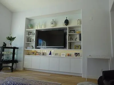 White built-in entertainment center with shelving, TV niche, and lower cabinets in living room