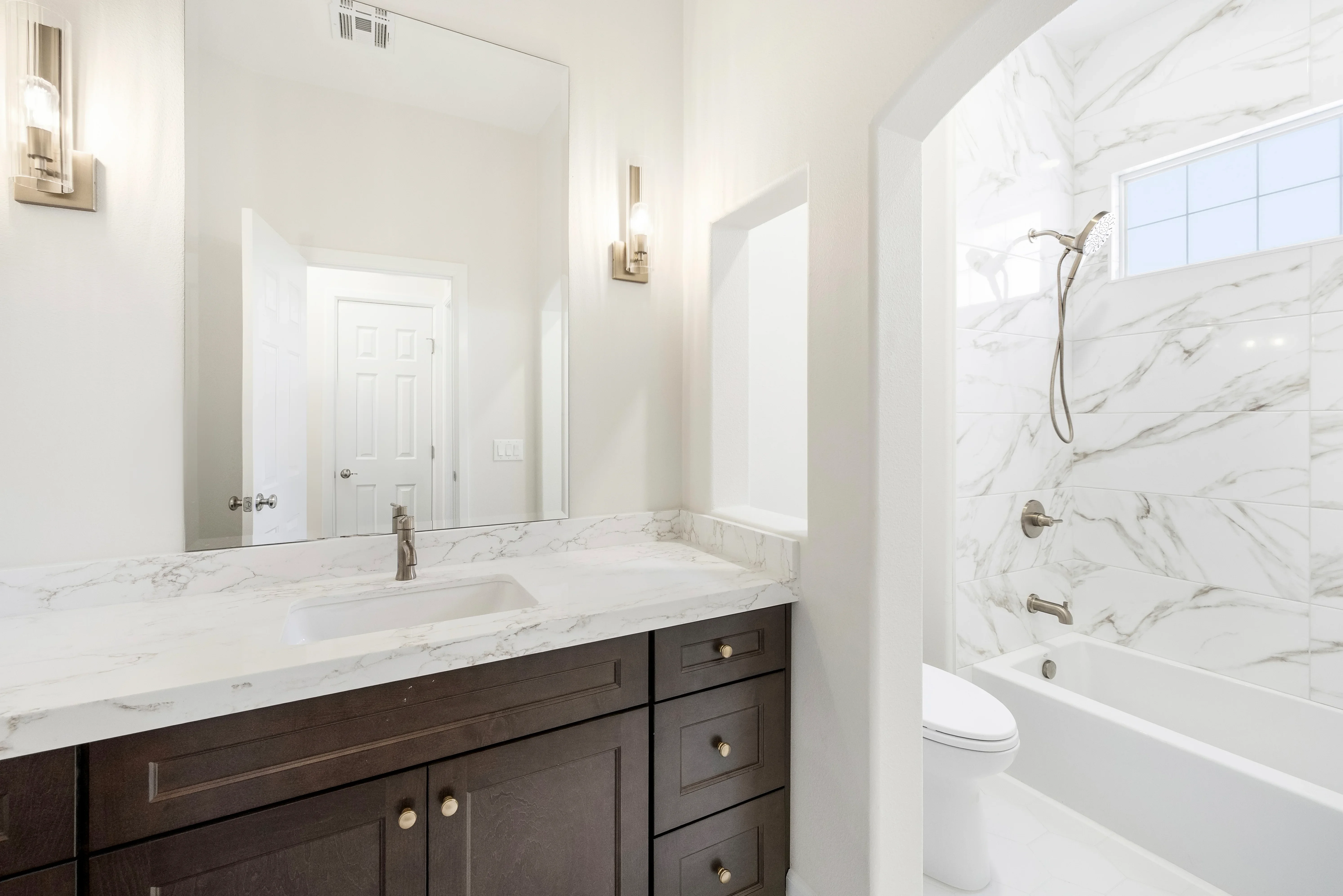 Marble countertop bathroom with dark wood vanity, marble tile shower, and framed mirror