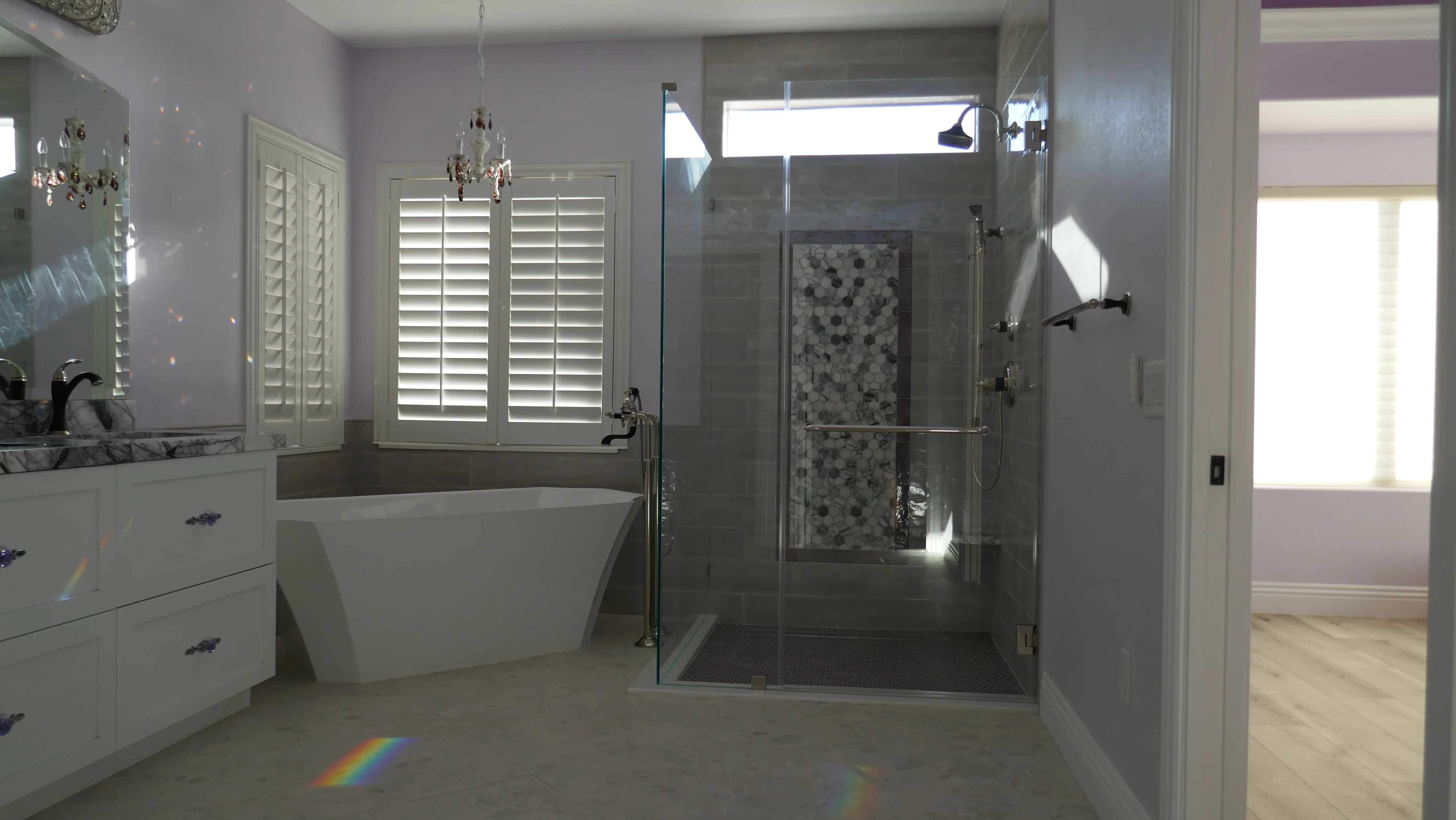 Master bathroom with freestanding tub, frameless shower enclosure, white vanity, and marble tile work